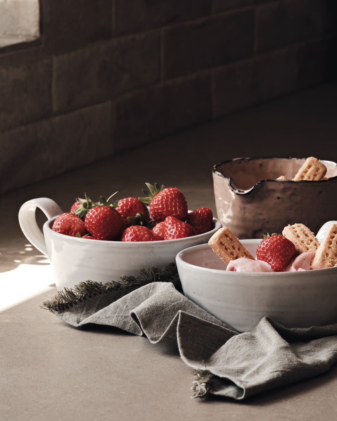macro image of pink ice cream scoops in white bowl with shortcake biscuits and strawberry garnish, muted summer light