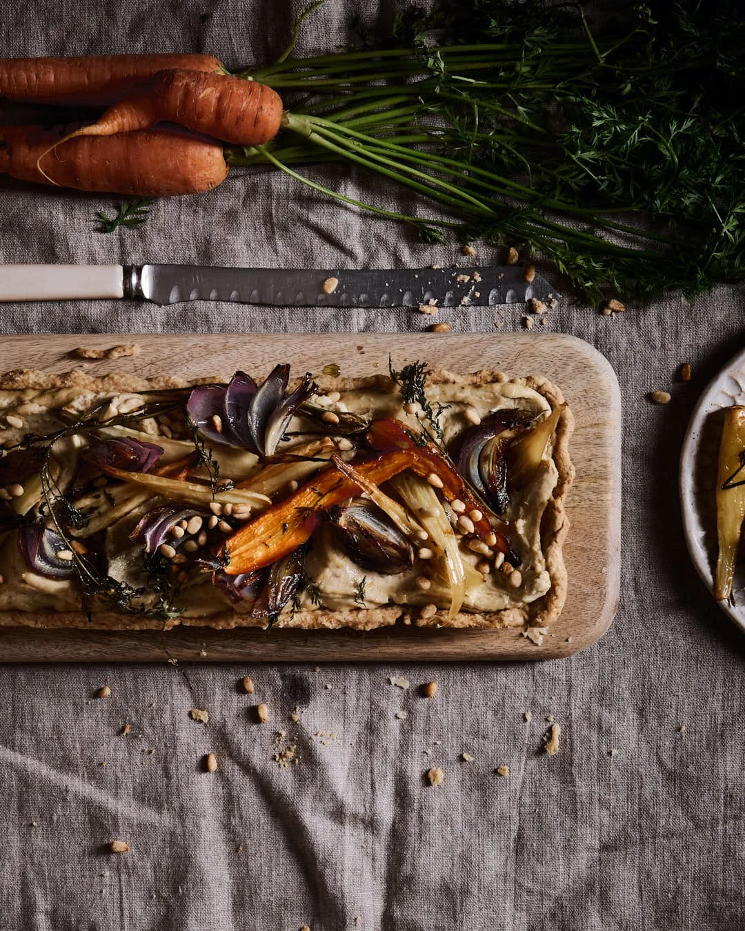 flatlay iage of long tart with hummus and roasted root vegetables in moody winter scene with carrots