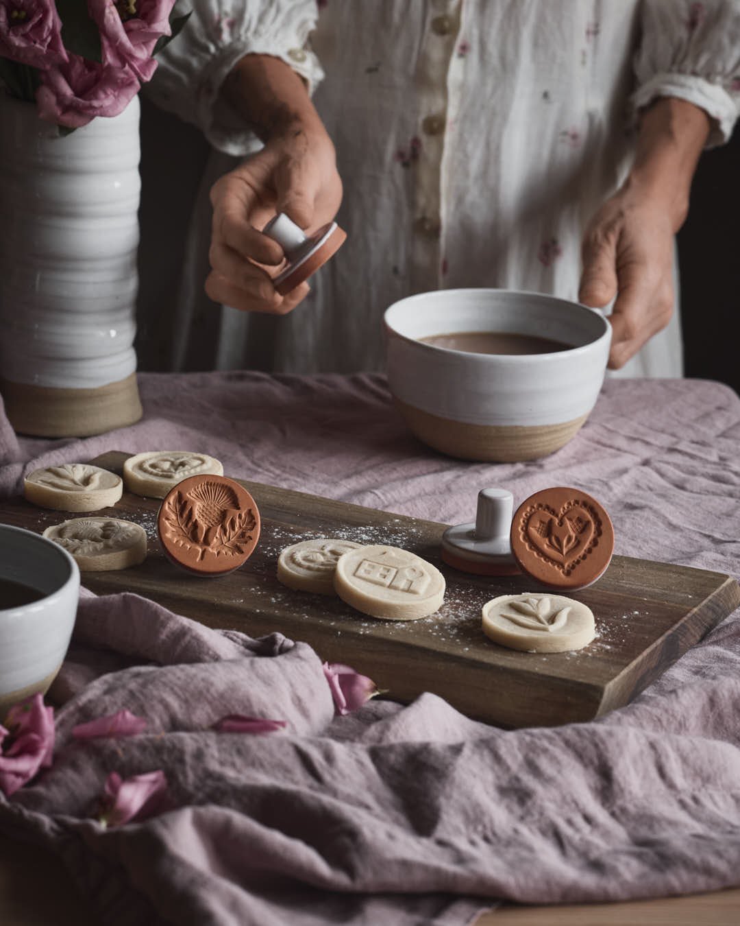 angled image pink tablecloth with platter of stunning shortbread cookies, with stamped designs in vintage romantic scene with pink petals