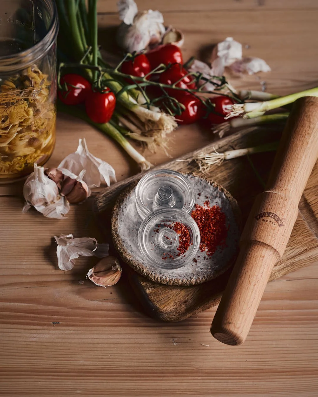 angled straight on image of glass jar of kimchi with chopping board and ferment presser in farmhouse scene