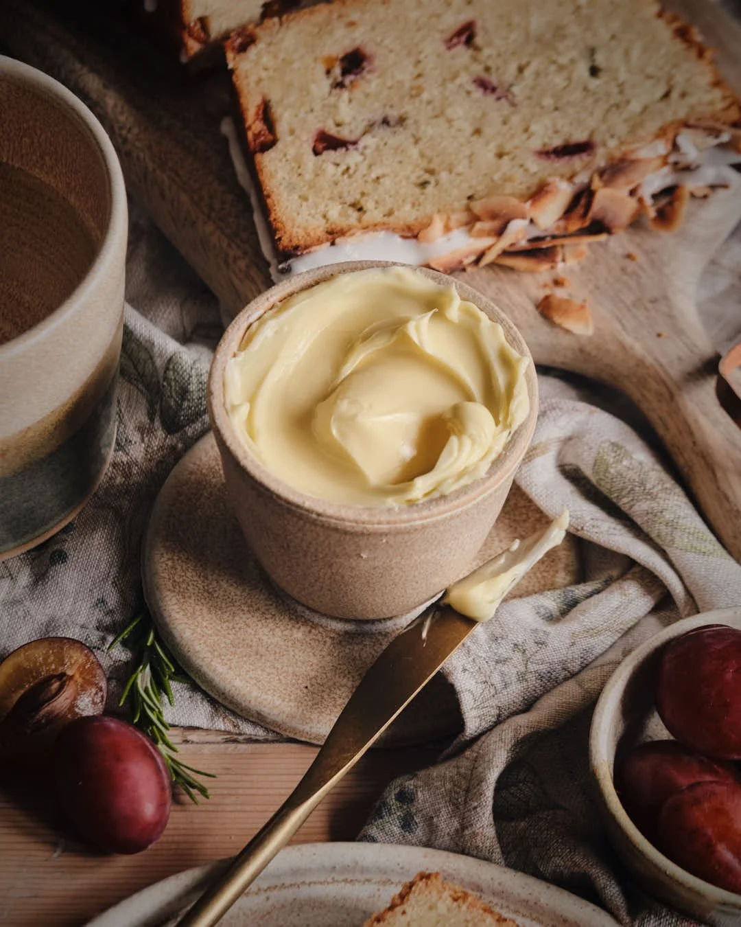 macro image of butter in butter  crock with knife and plums to surround