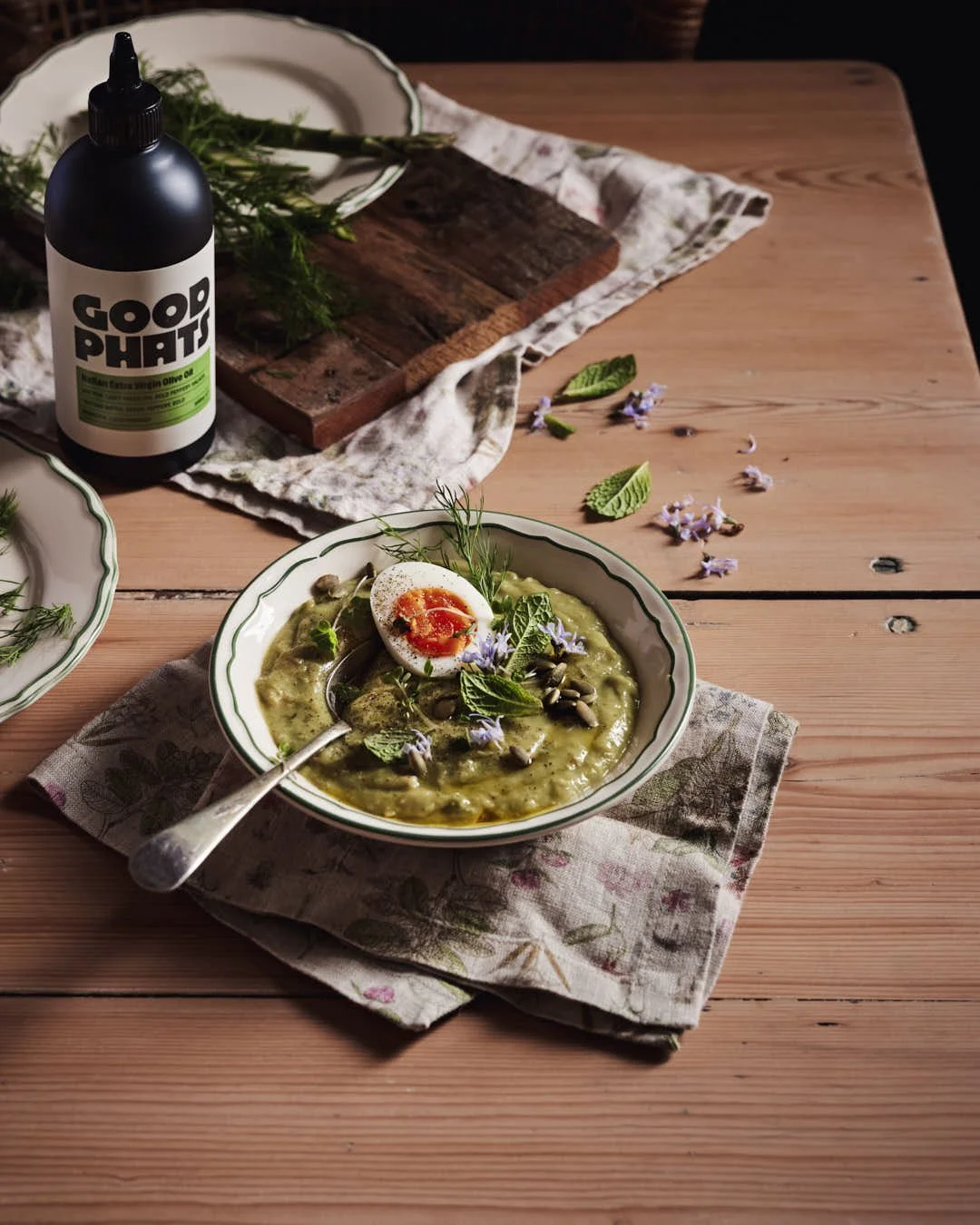 angled image of olive oil being drizzled onto green soup in rustic farmhouse setting