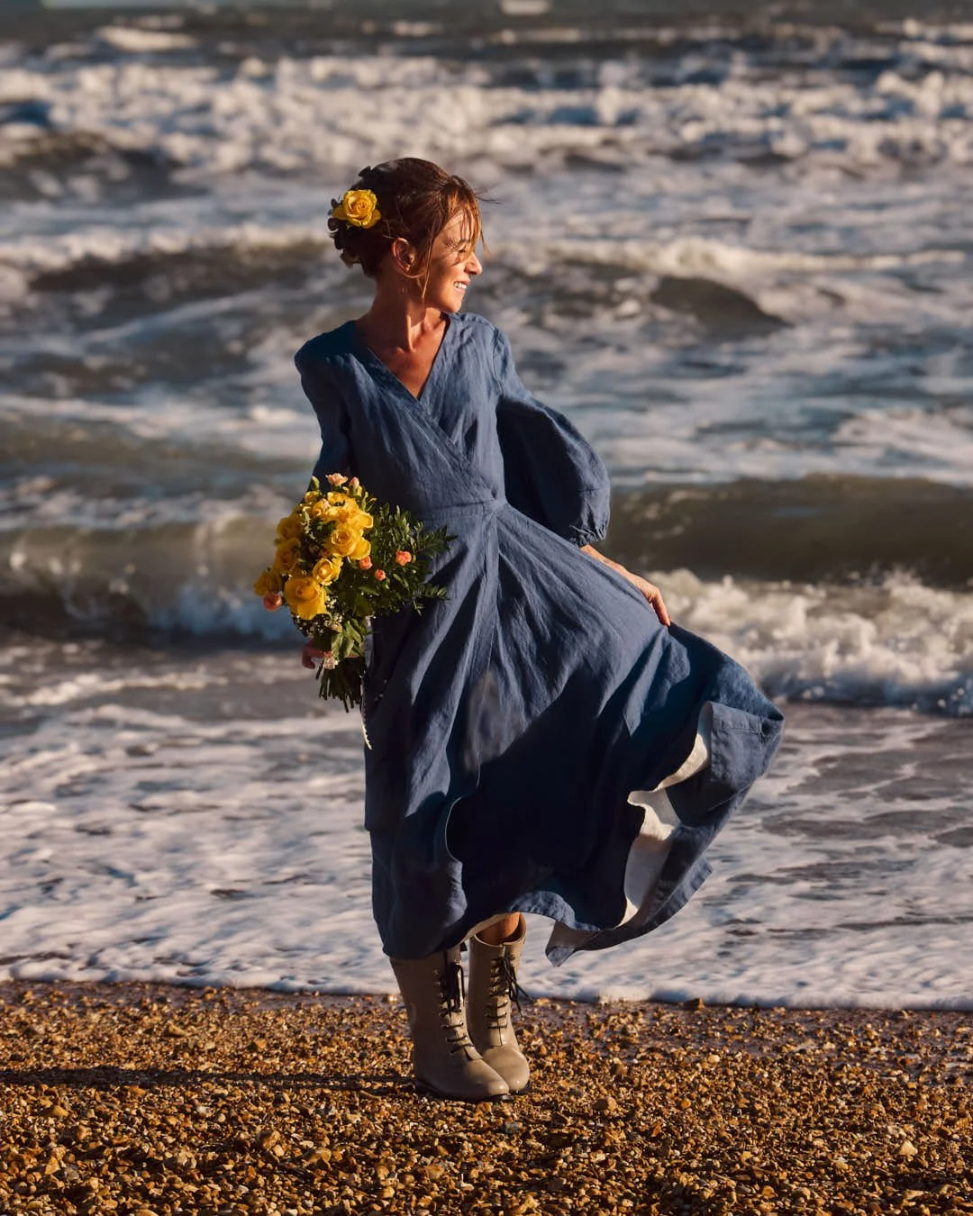 girl in muted blue dress on beach with yellow flowers in stunning winter sunlit scene