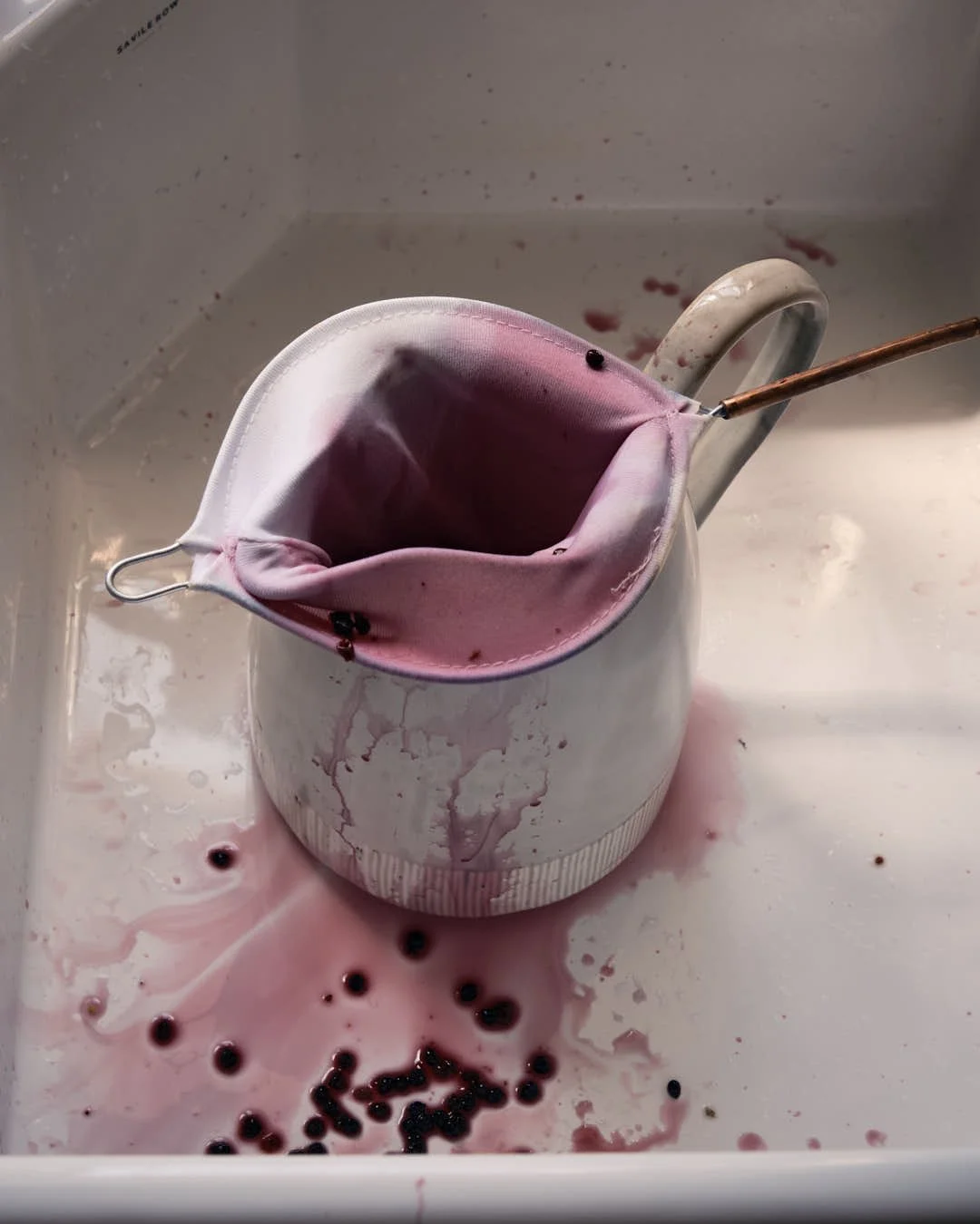 jug with stained cloth in sink with splatters of elderberries in deep purple