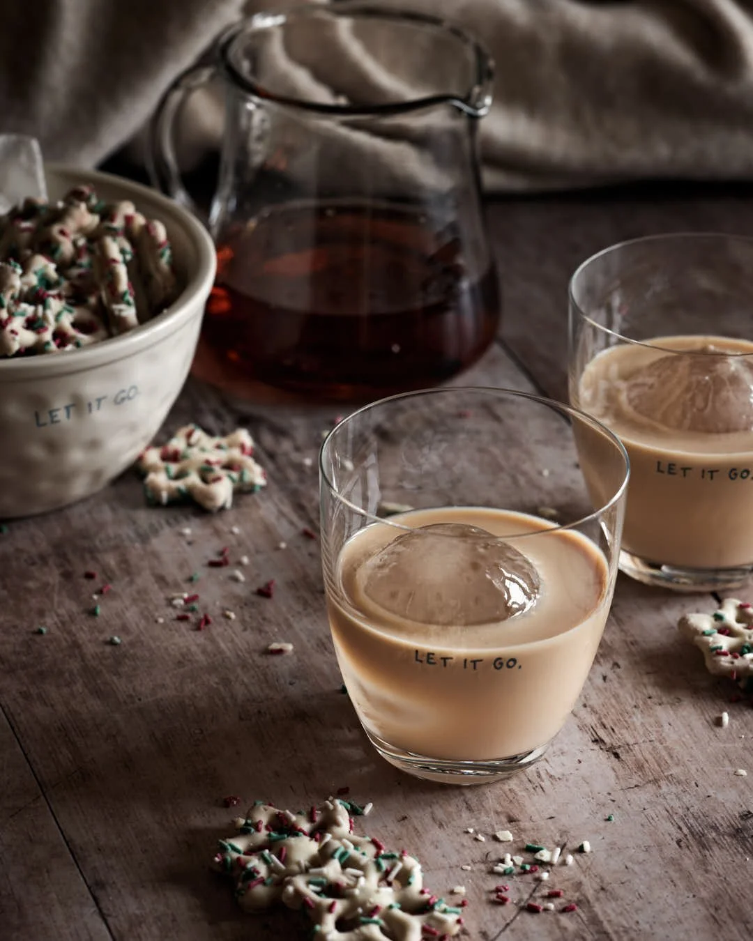 angled  image of two glasses of rum cream on worn wood surface in winter table scene with girl in cream sweater to back