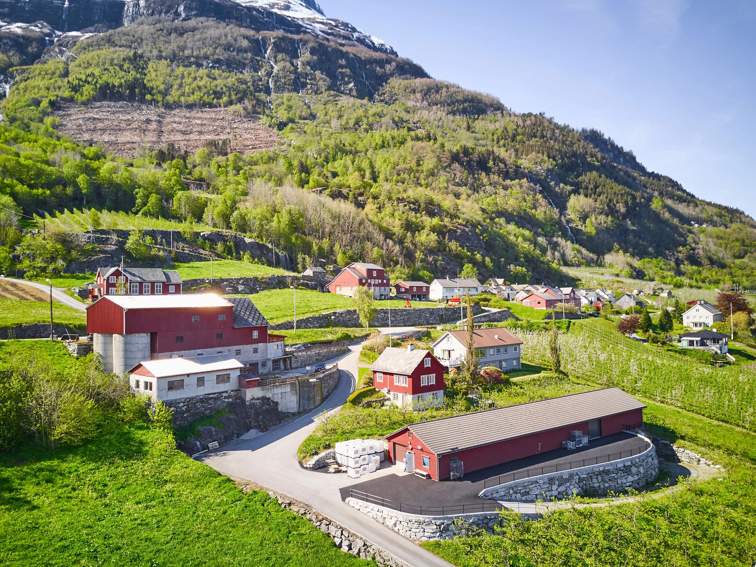 Flyfoto fra Aga, oversikt over gården, røde bygninger med en fjellside bak, sommerdag