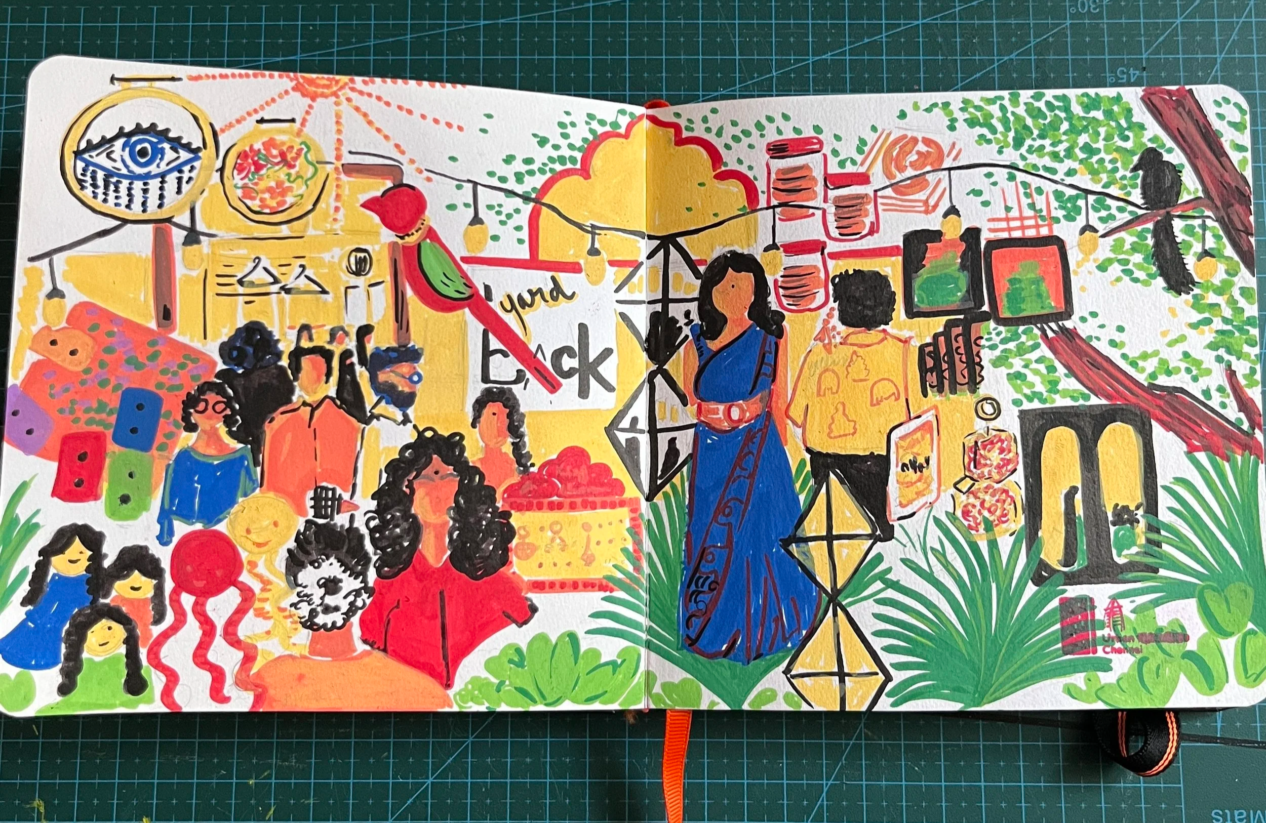 An urban sketch made with pencil and acrylic marker of an art event in Chennai featuring people exploring the market, some products like embroidery art, resin art, a big red parrot, some cookies and desserts, and some colorful cassettes 