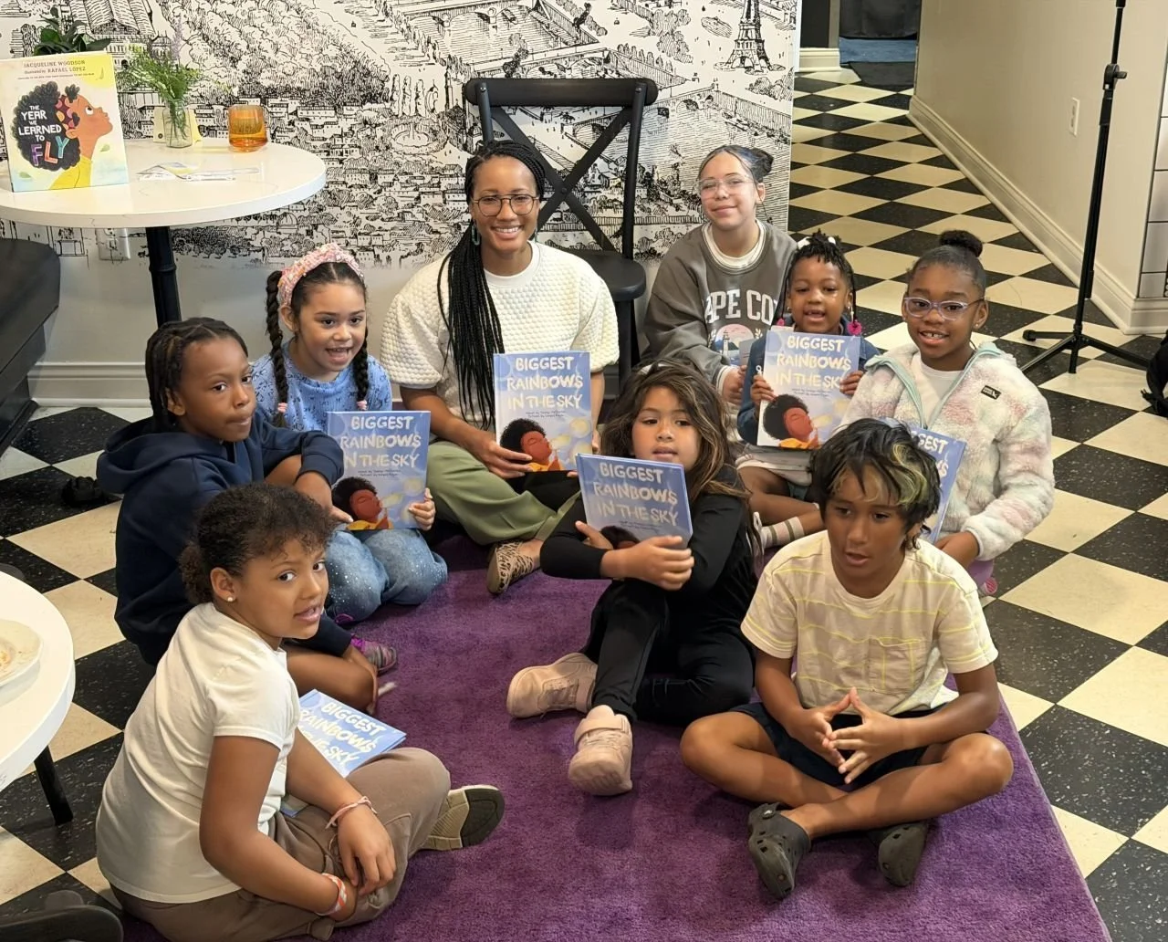 The author of Biggest Rainbows in the Sky, Jocelyn Mcquirter, is at a reading, surrounded by children who are reading along with her