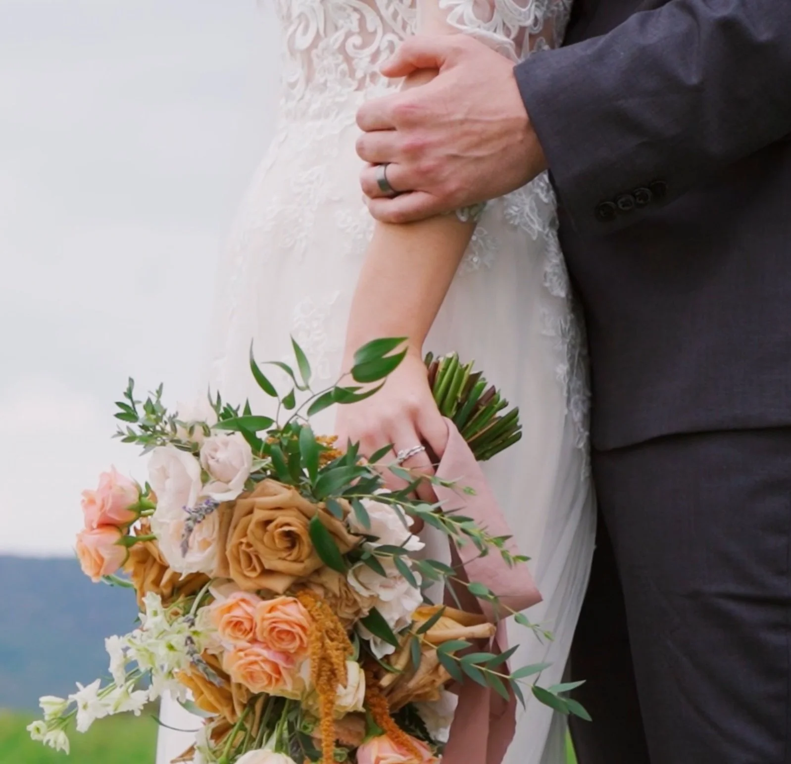Close-up of a bride and groom holding hands with a bouquet of flowers.