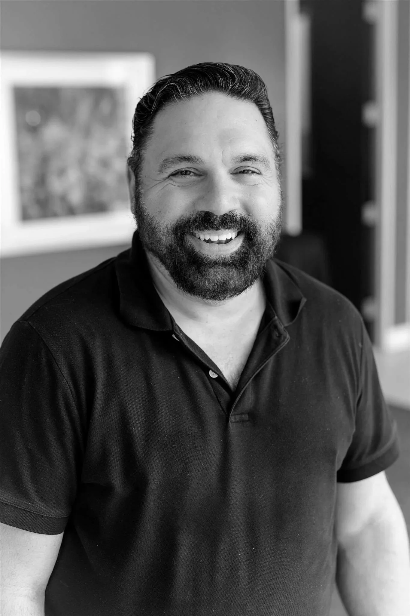 Black and white photo of a smiling man in a dark shirt in front of a geometric background.