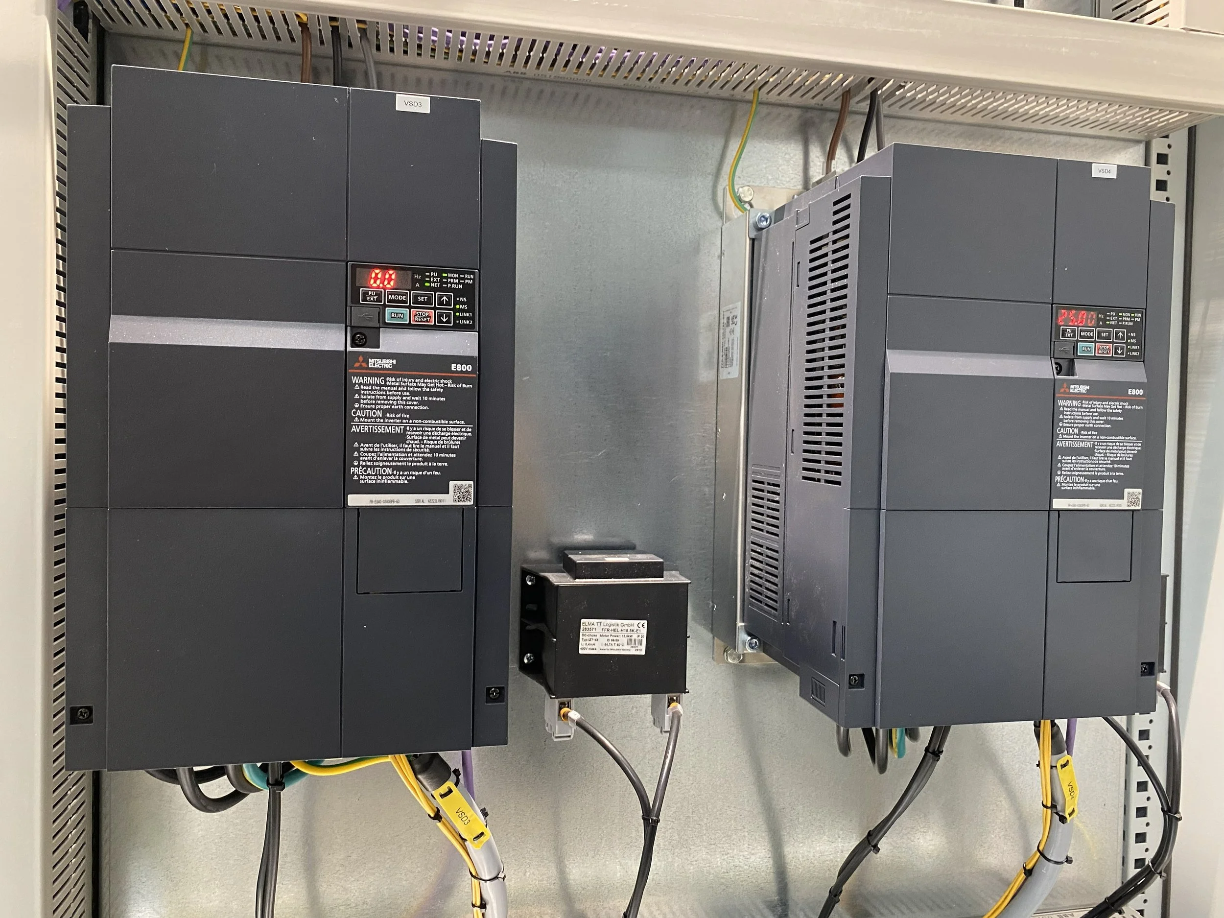 Two industrial drives mounted on a wall with wires connected, alarm indicator lights on, and a small black communication device in between.