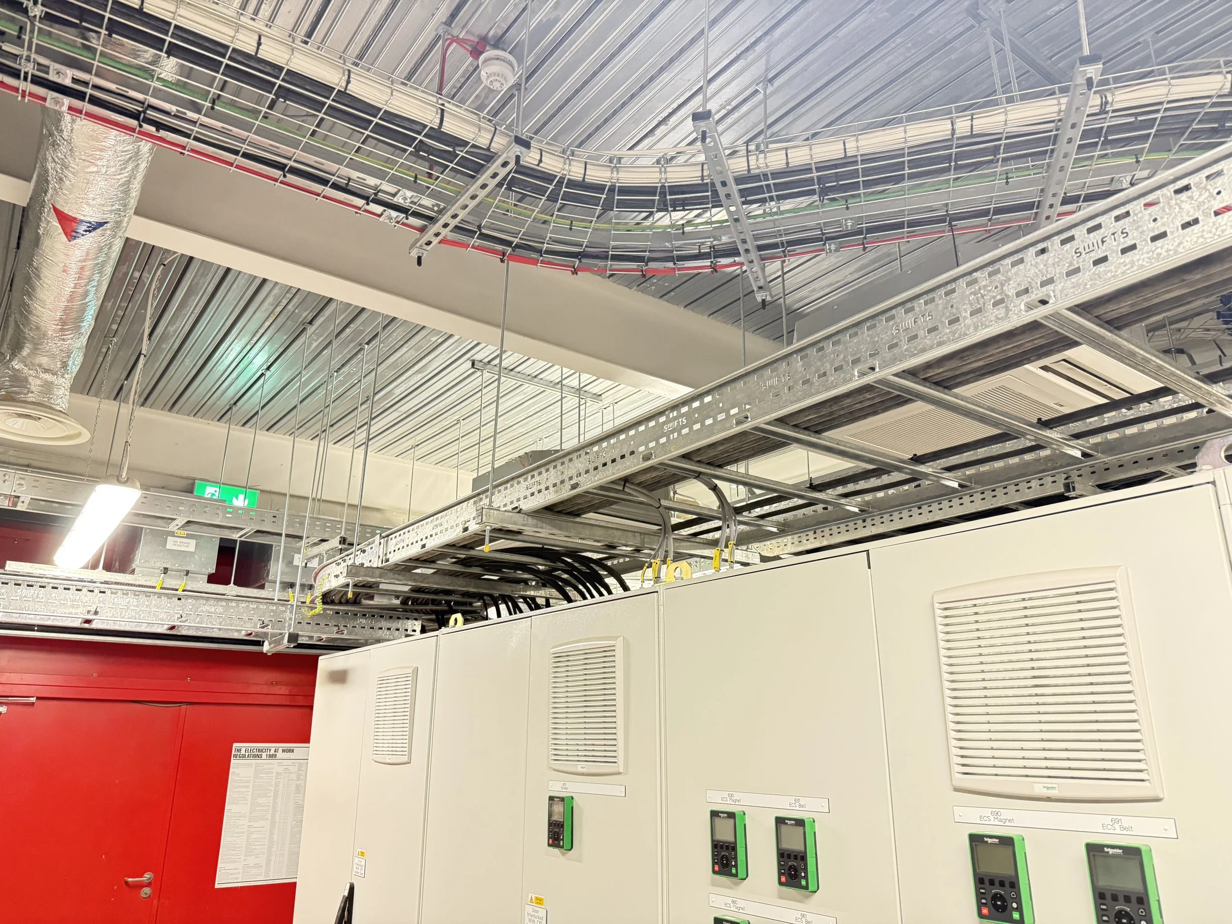 Ceiling with exposed metal ductwork, electrical cables, and control panels in an industrial or commercial building.