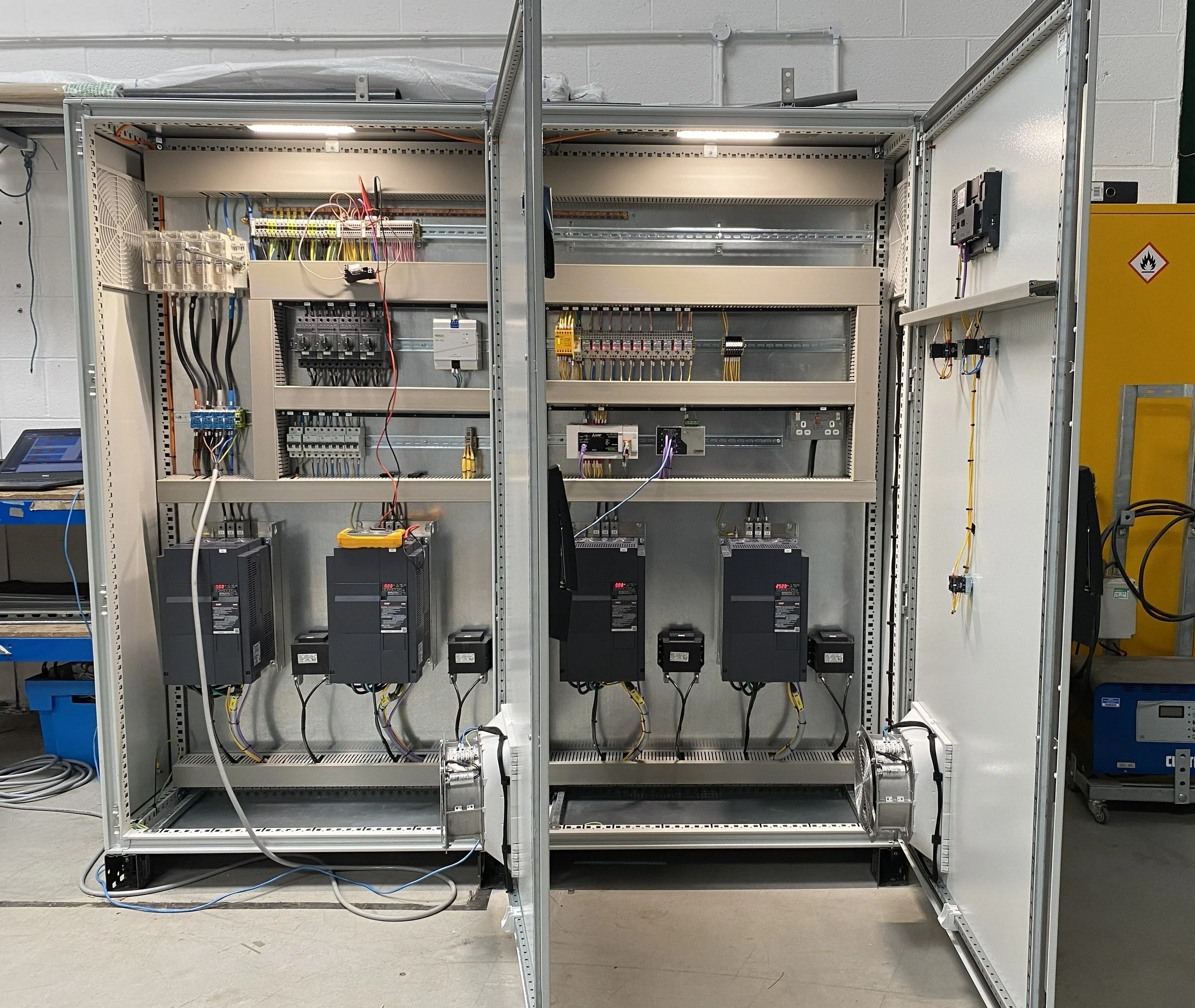 Unfinished electrical control panel with various wires, circuit breakers, and electronic components inside a metal frame.