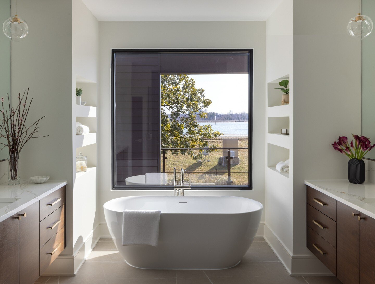 Hard to beat the water view from this tub!  Swipe to see the incredible shower too👉. A few next level details we considered when designing this bathroom: large format textured tiles, floating walnut vanities, wall mounted faucets and plenty of mod s