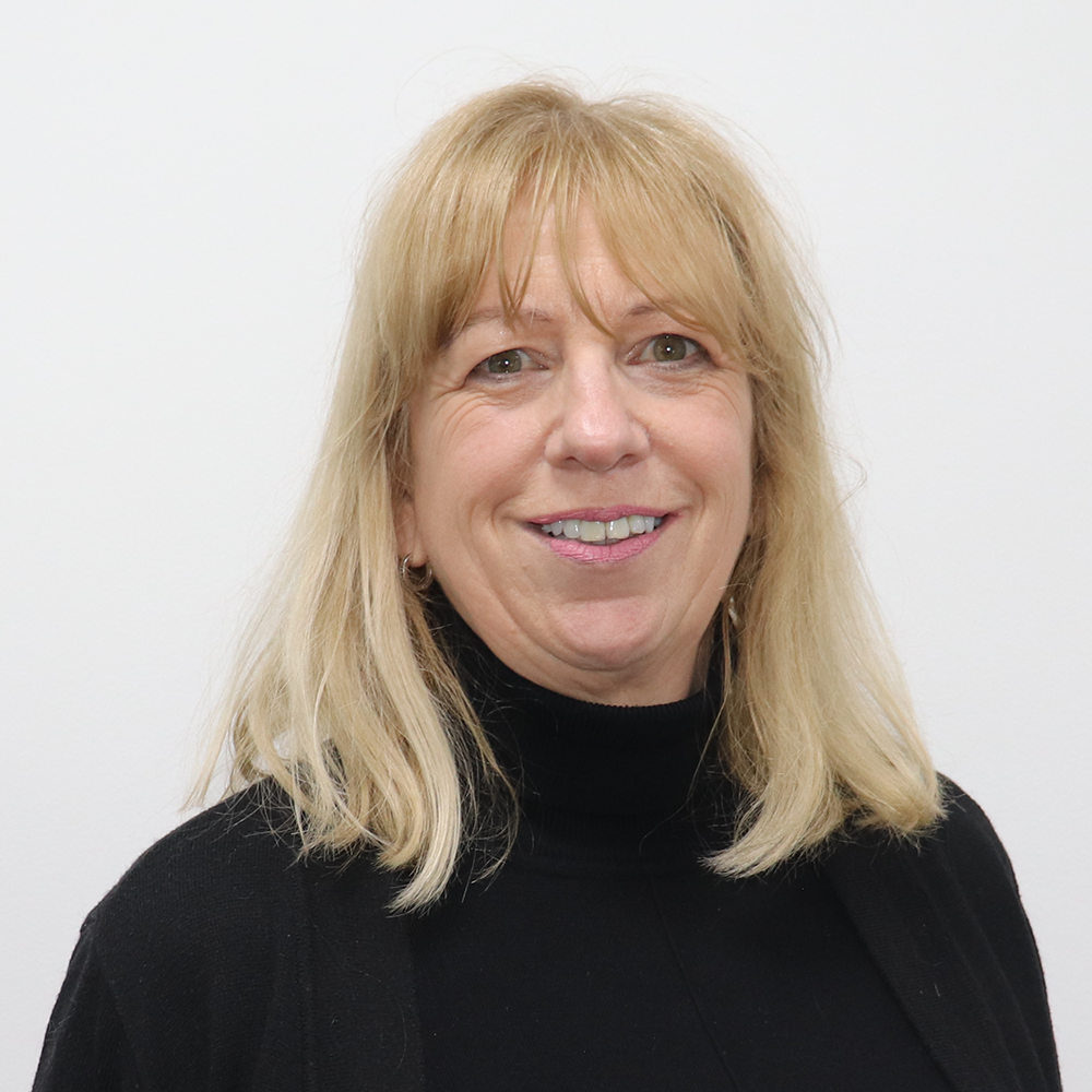A smiling woman with blonde hair, wearing a black turtleneck, against a plain white background.