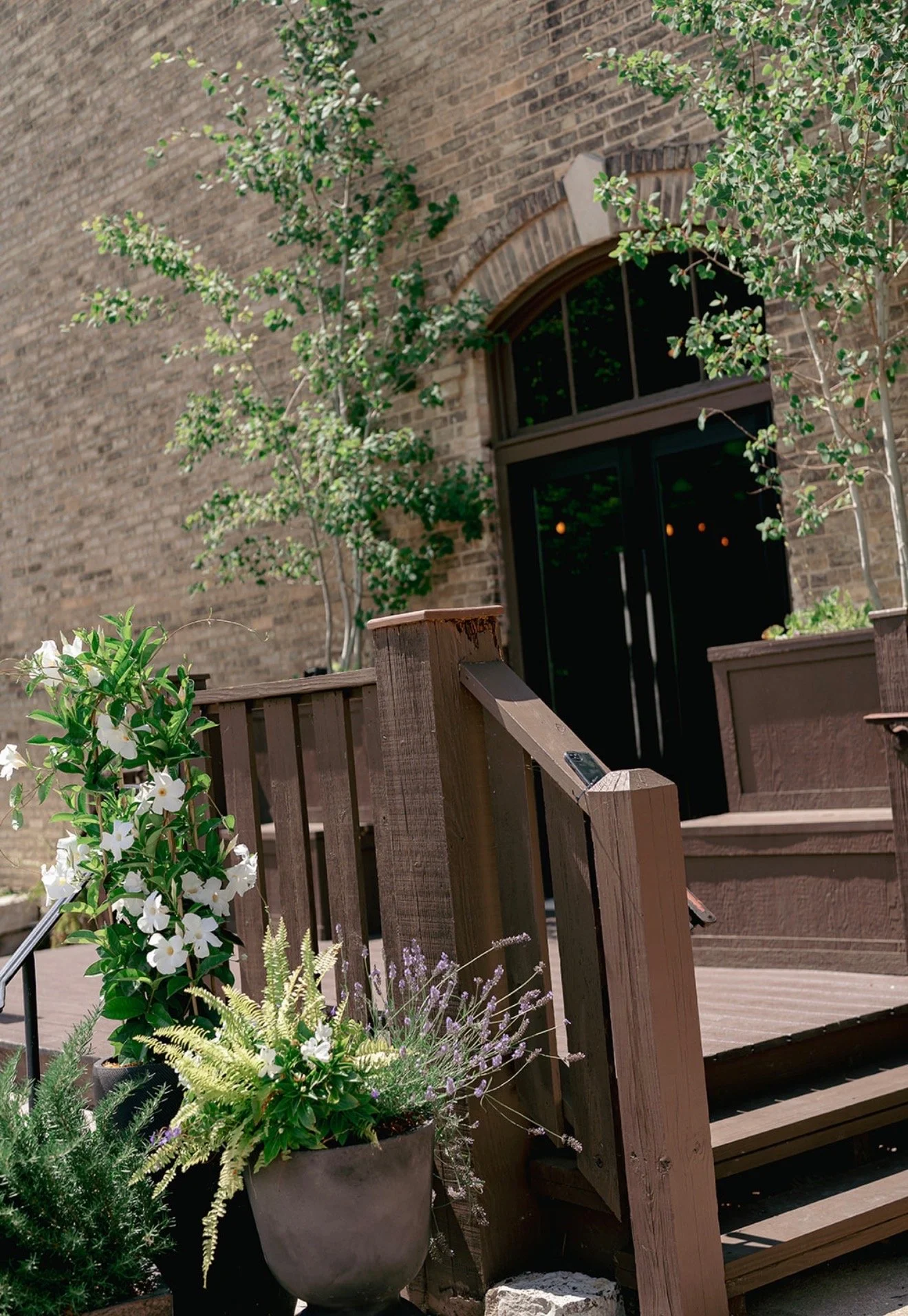The Lageret outdoor brick entrance with wood deck  surrounded by beautiful greenery and summer florals