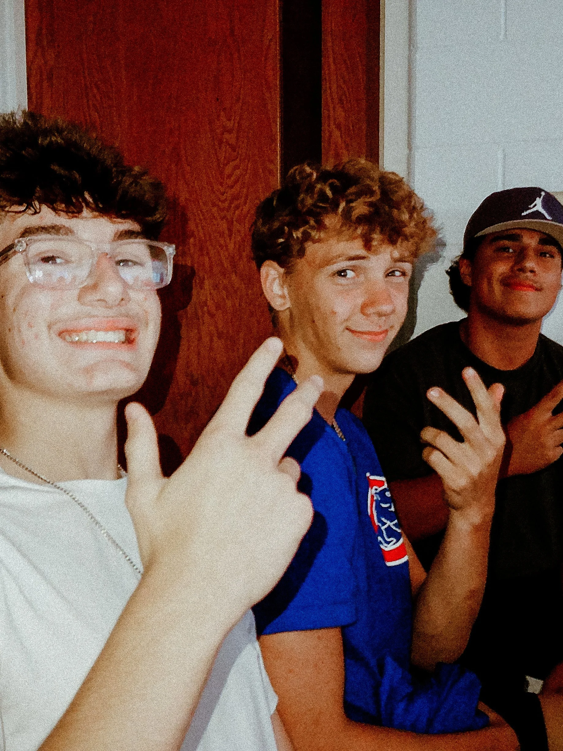 Three young men taking a selfie together, smiling, with one showing a peace sign.