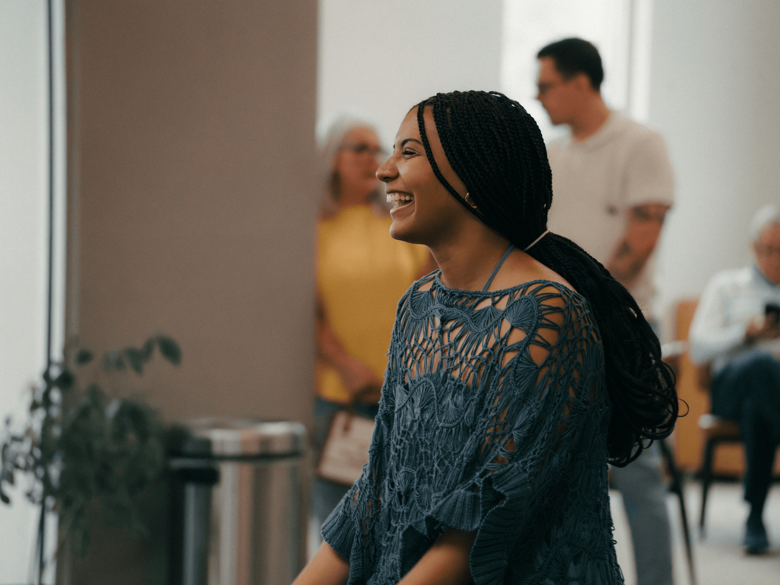 A woman with braided hair smiling at a social gathering inside a bright room, wearing a blue, patterned top. Christ's Family Church Davenport Iowa