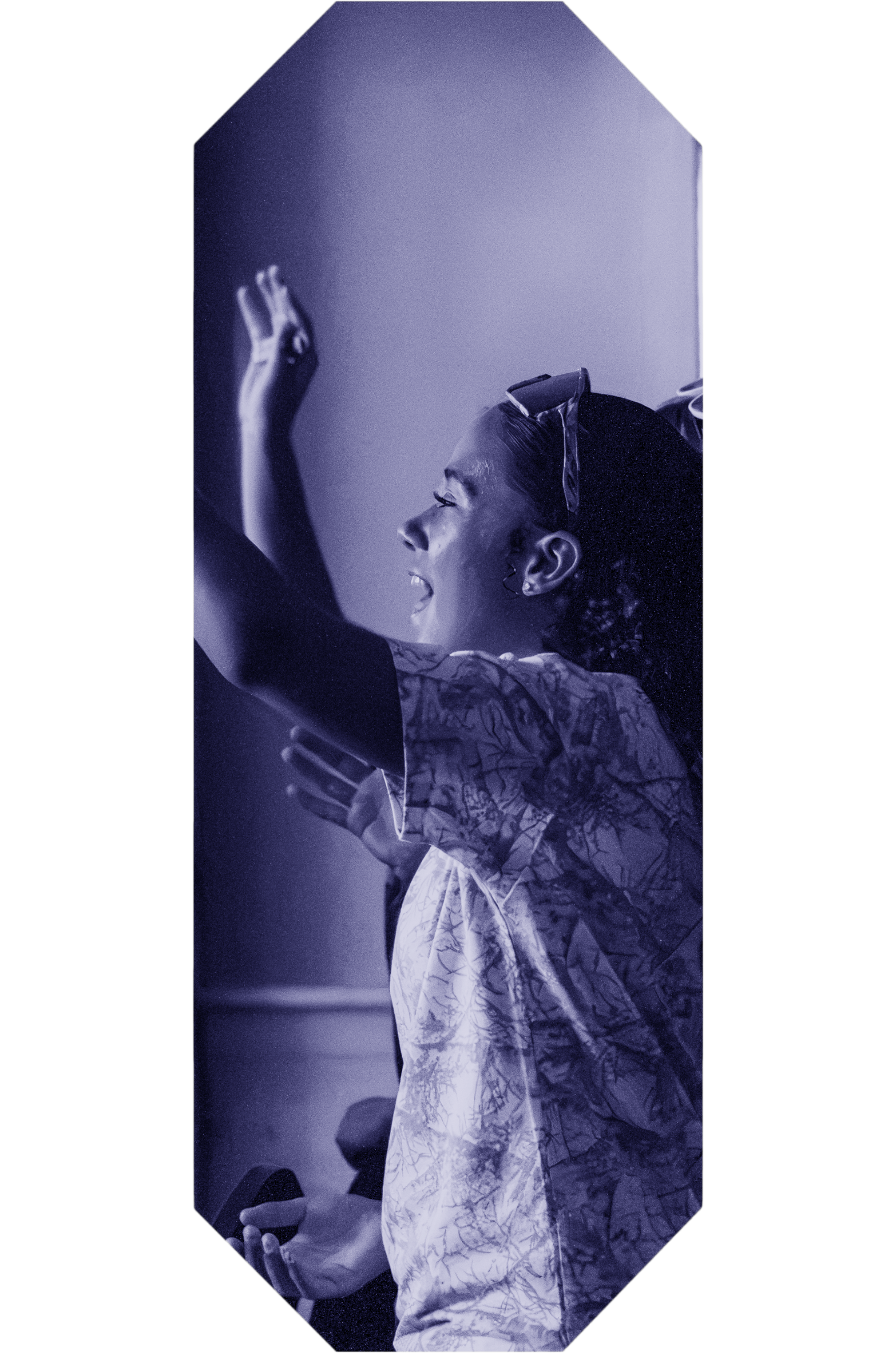 A young woman with braided hair and hoop earrings, wearing a patterned dress, taking a selfie with her smartphone in front of a mirror, illuminated with purple lighting.