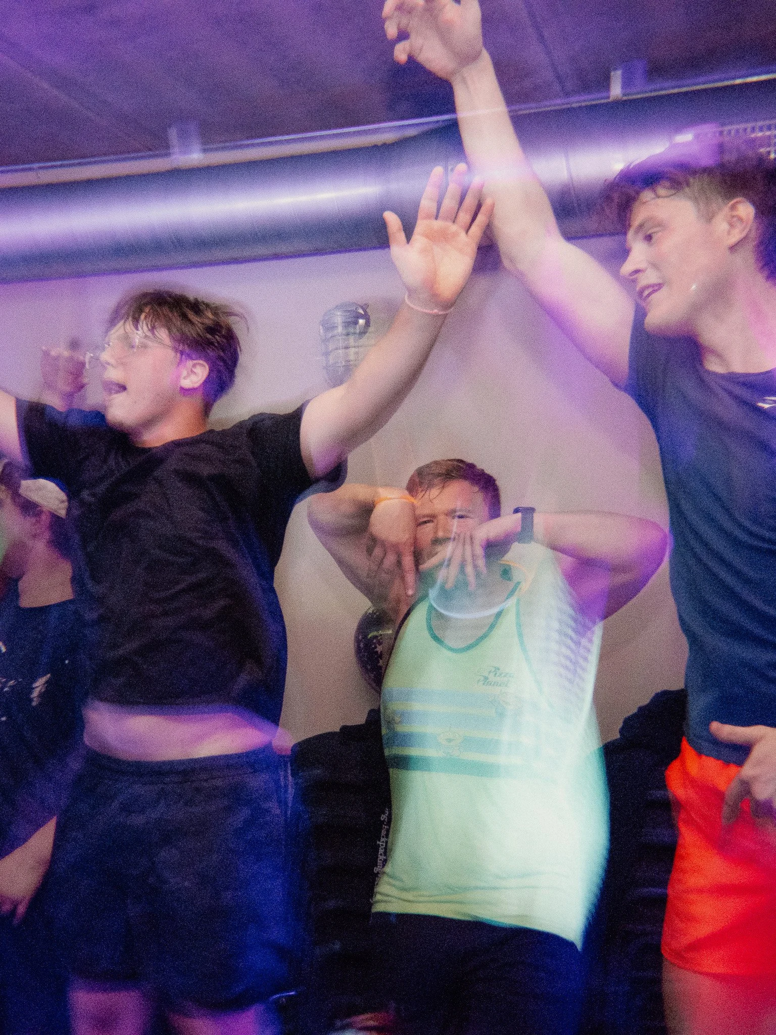 Three young men celebrating and dancing at a party with colorful lighting.