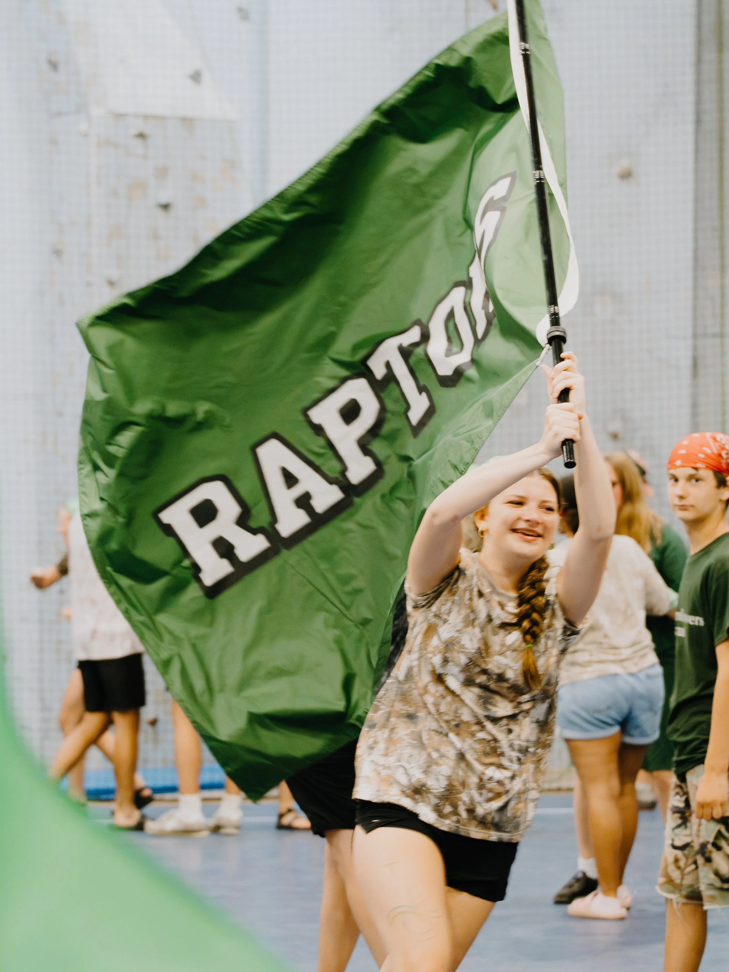 Young girls dancing and holding a green flag with the word 'PRIDE' on it in an indoor gymnasium.