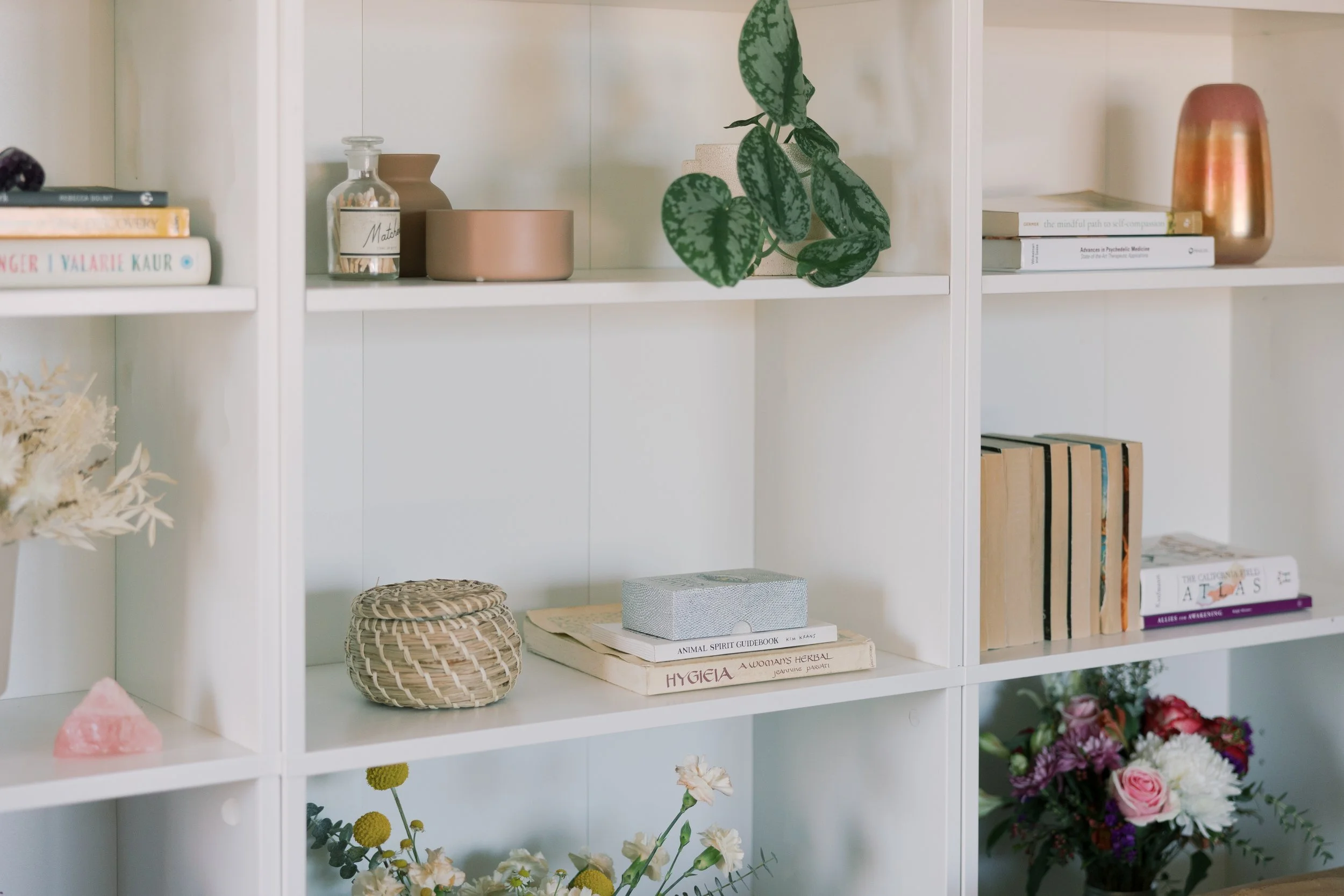 A white bookshelf with decorative objects, books, a potted plant, and flowers.