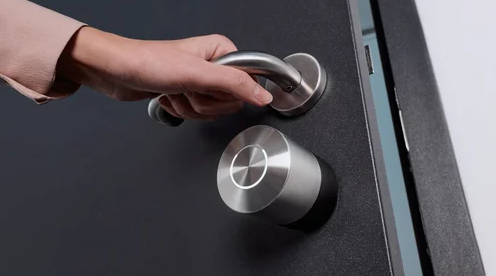 A person turning a silver door handle on a black door.