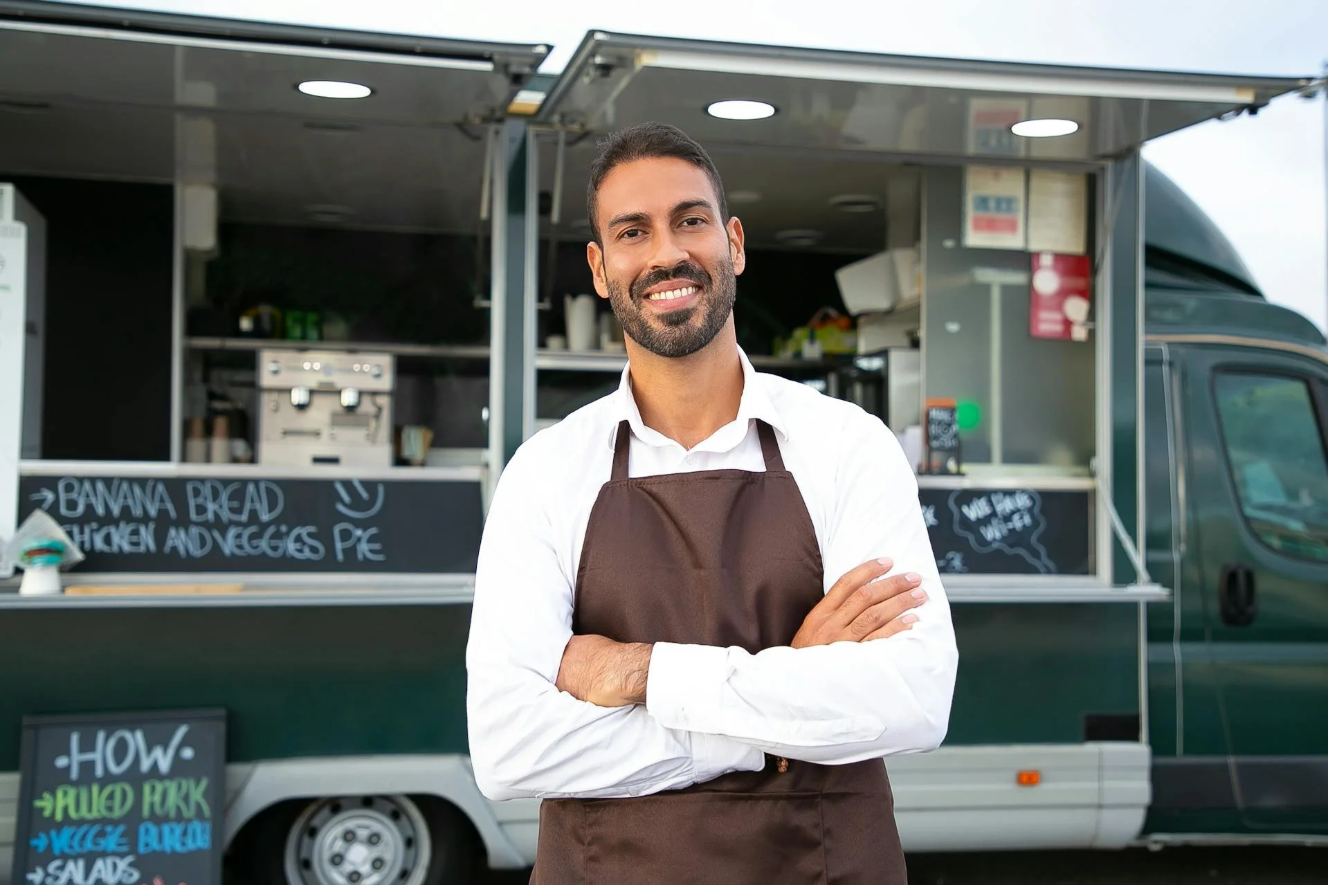 a business owner stands in front of his food truck, arms crossed with a smile. He worked with a waterloo financial planner at GRFS to help keep his business afloat when he was on the brink of corporate bankruptcy.
