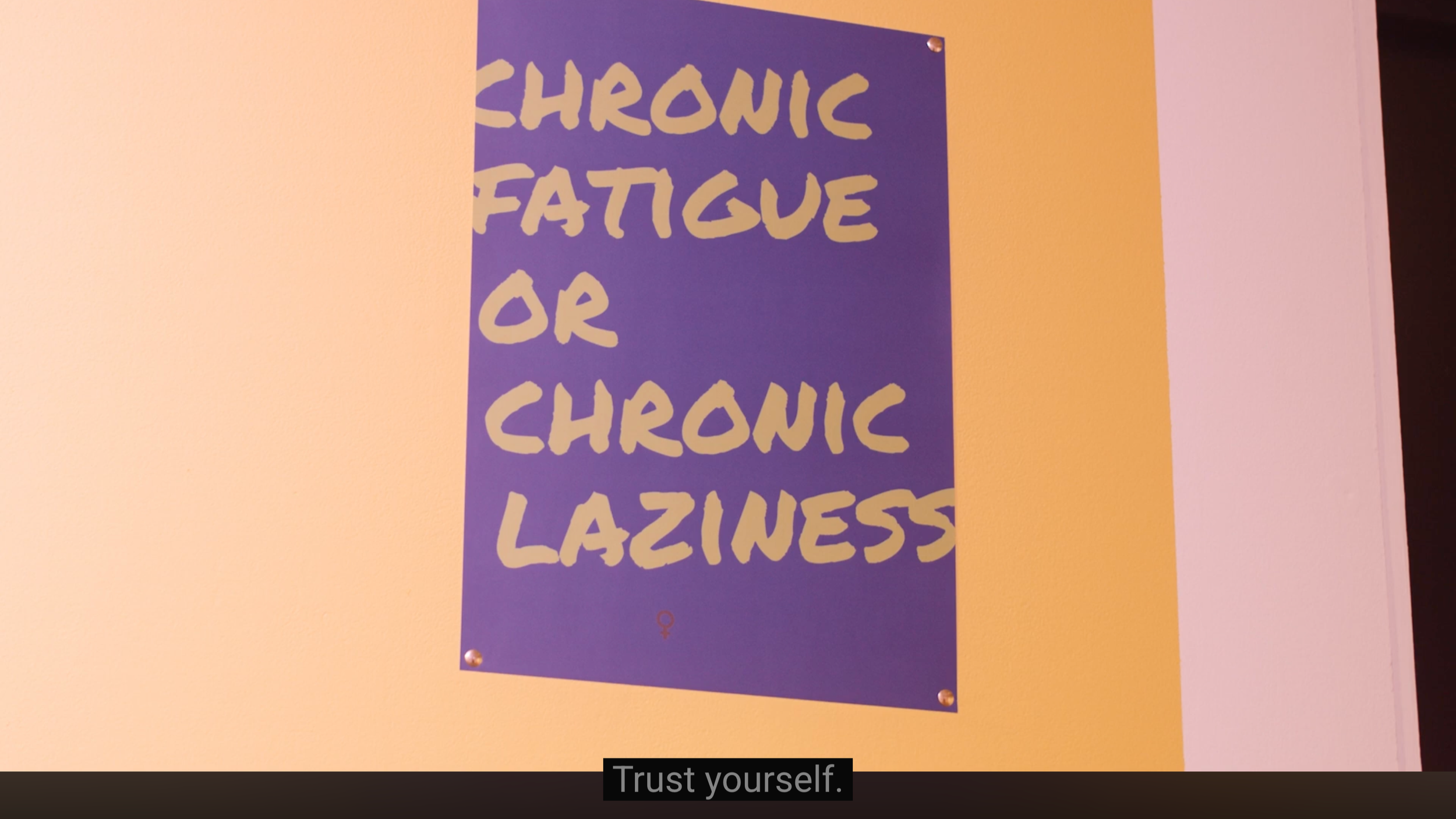 Close up of Blue Poster on a yellow wall in the 'waiting room'. Green type reads: Chronic fatigue or chronic laziness?'
Subtitle below video reads: Trust yourself.