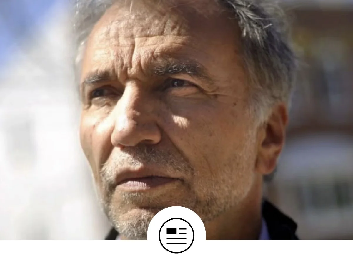 Close-up of an older man with gray hair and beard looking into the distance outside, with sunlight on his face.