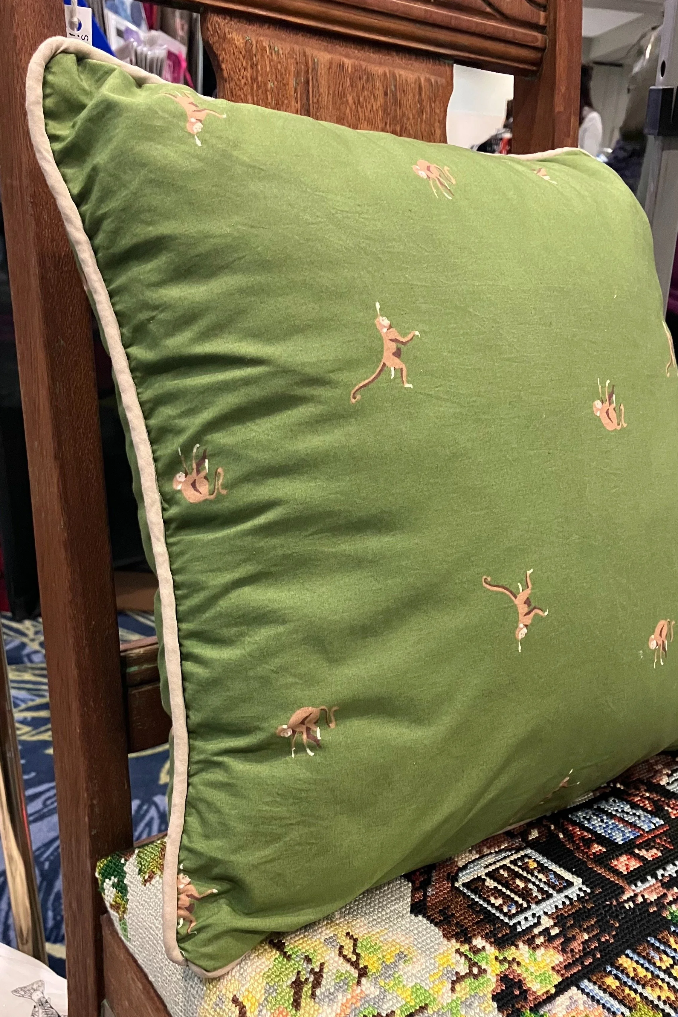 Olive green pillow with small monkey print and tan pipping.