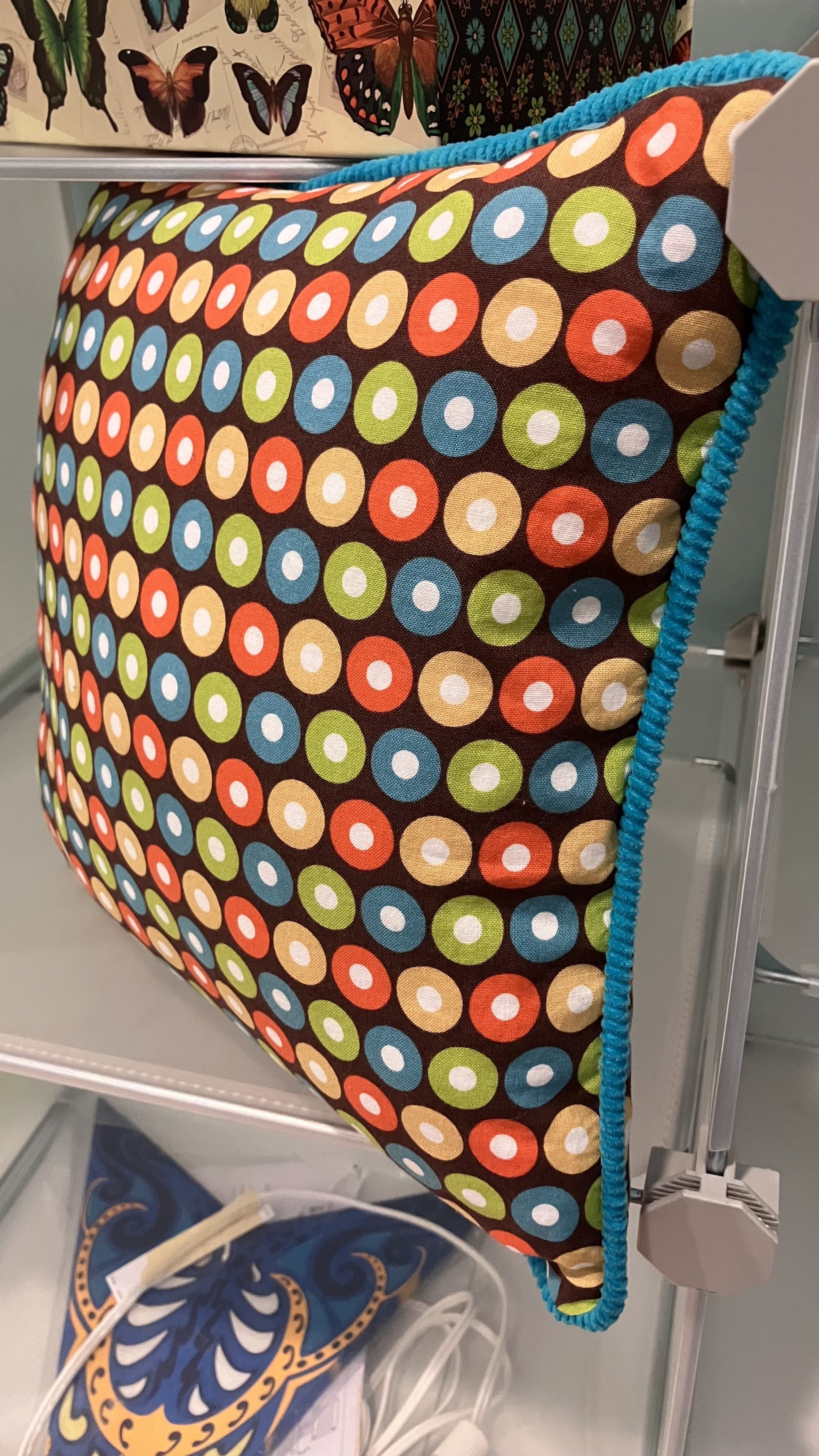 Pillow with teal blue corduroy pipping, and a brown print with orange, yellow, blue, and green polka dots.