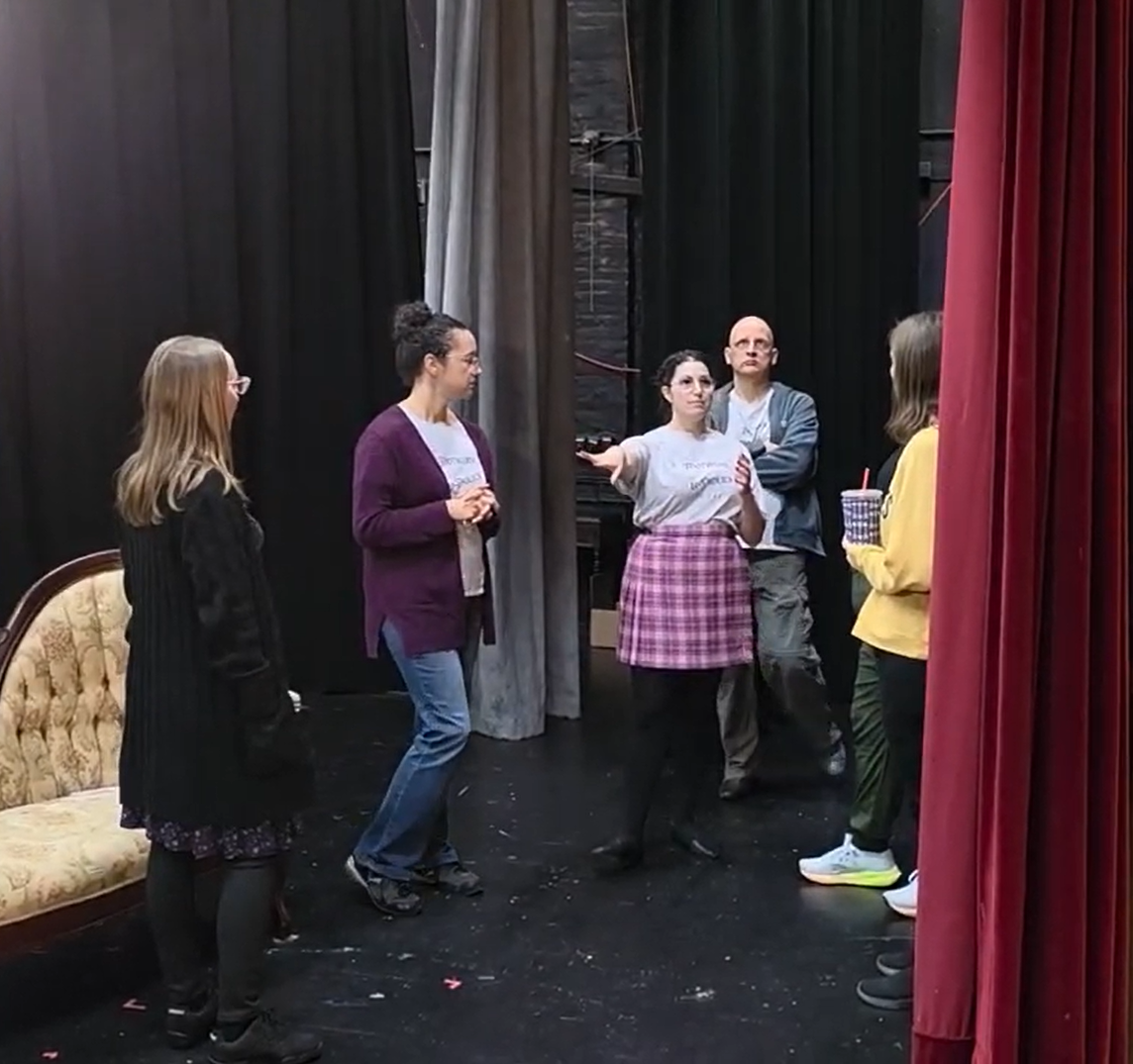 four members of footwork and frolick in conversation with hands actively gesturing, standing on a stage with a classic velvet curtain in front of them