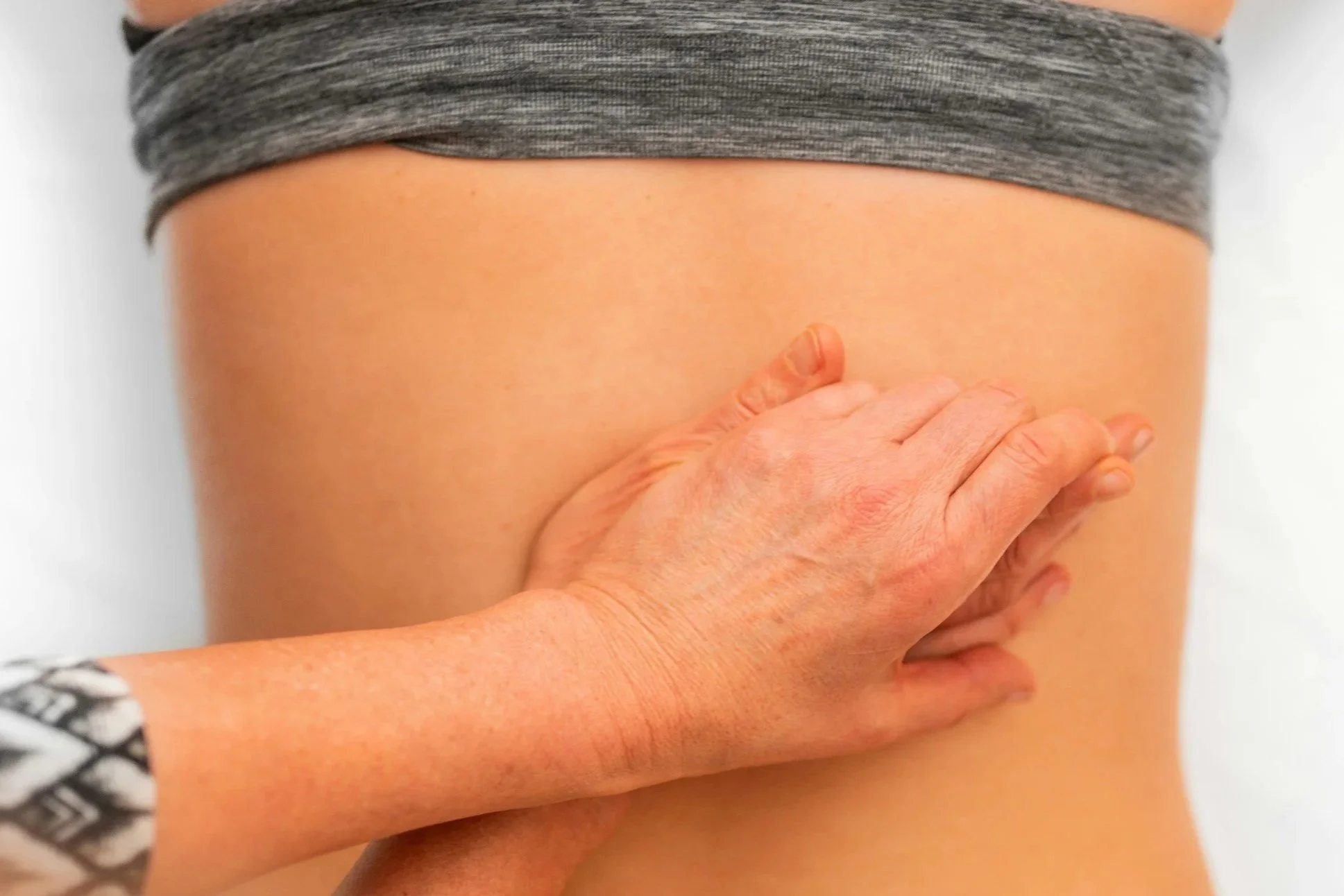 Close-up of a person’s hand touching their lower back, with a gray shirt rolled up above the waist.