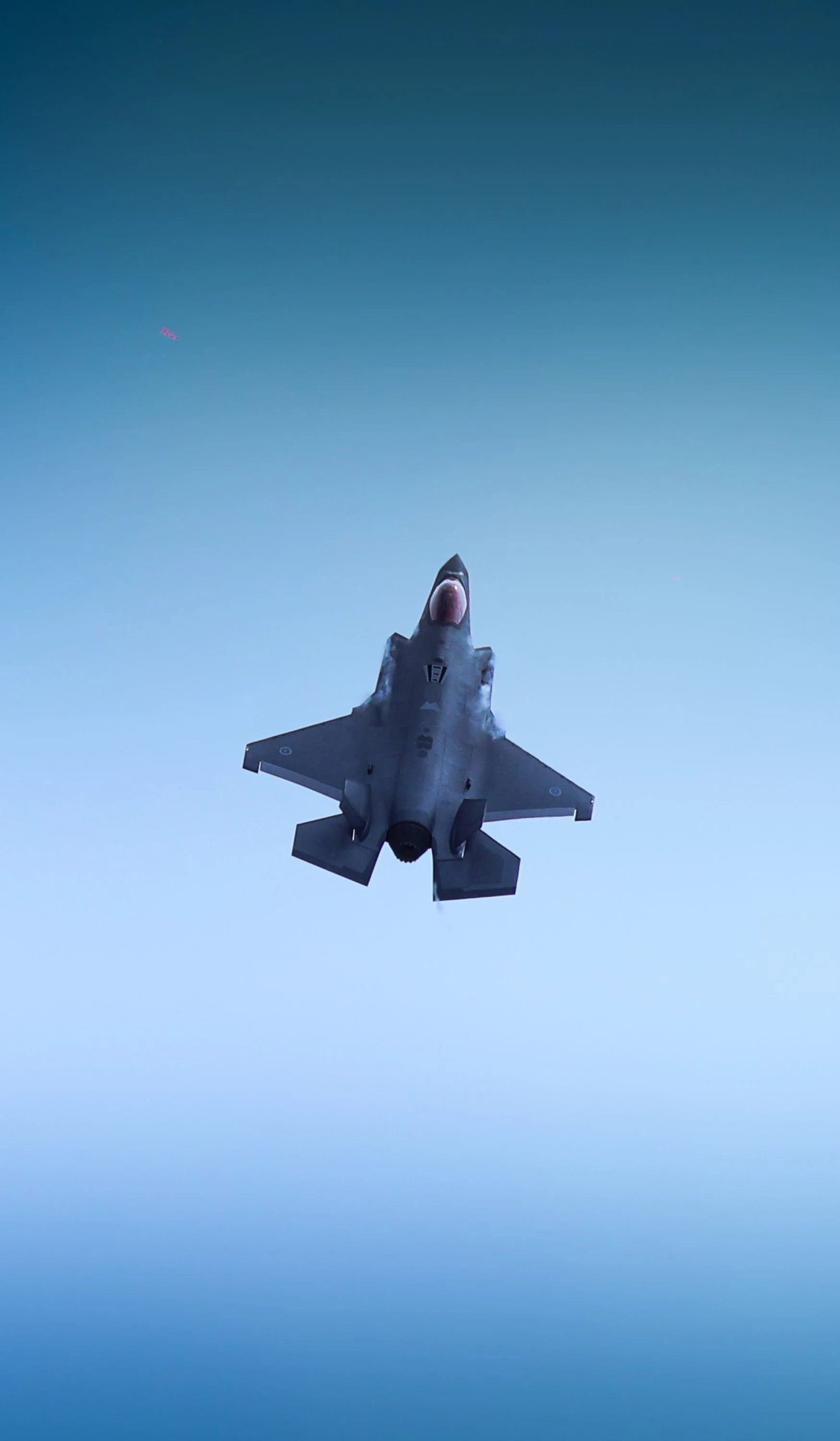 Military fighter jet flying at high altitude against a blue sky.