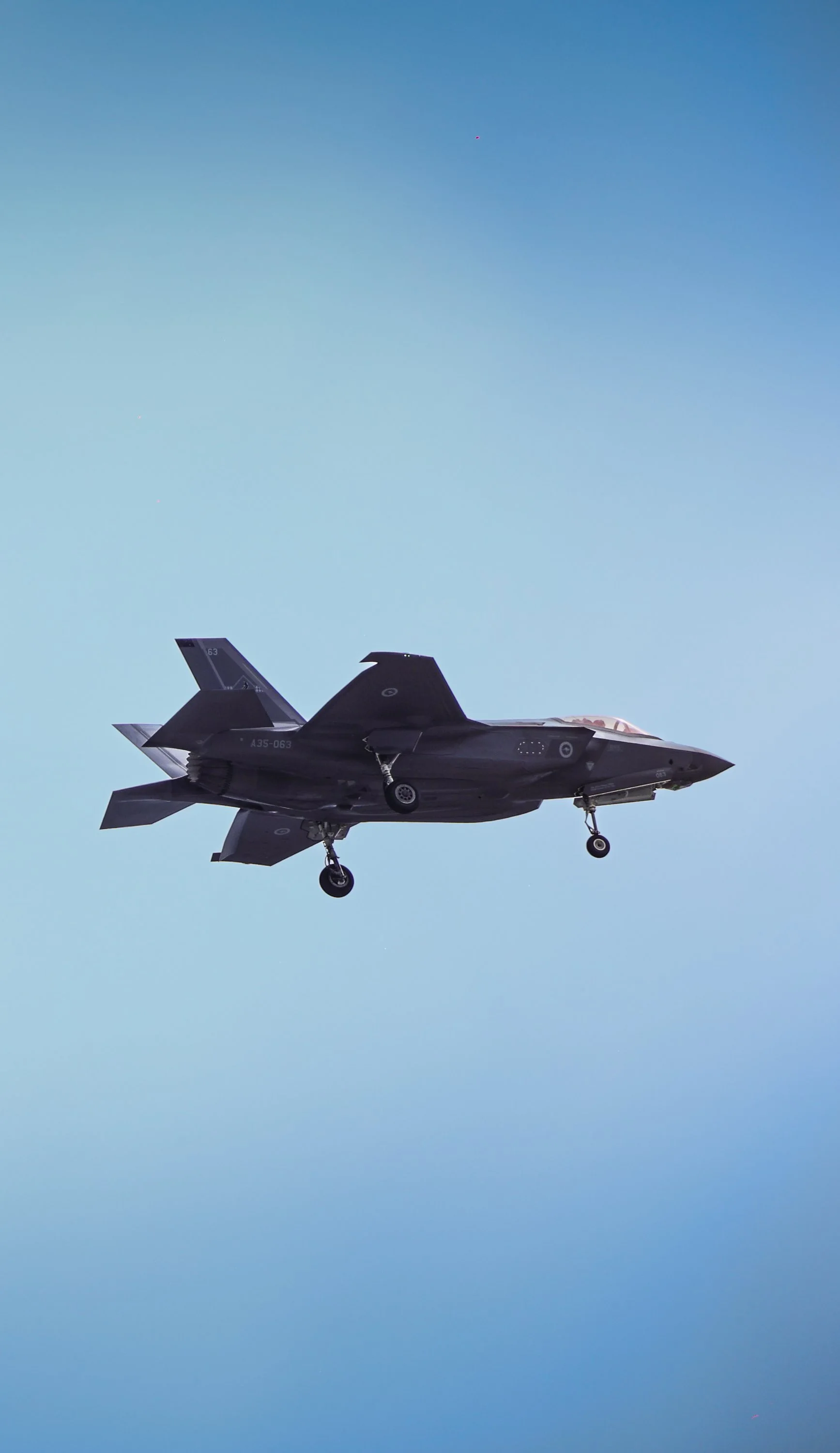 A military fighter jet flying in a clear blue sky with its landing gear extended.