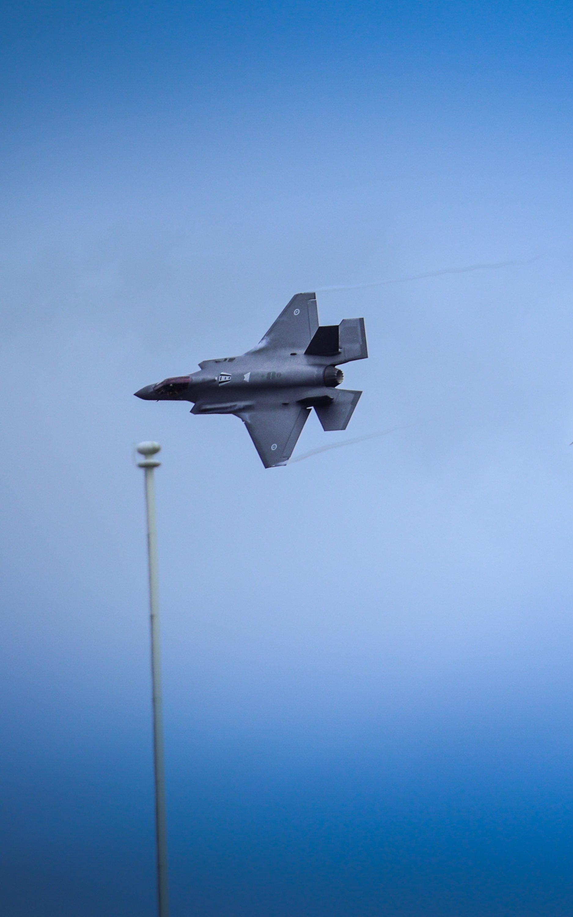 A fighter jet flying in the sky near a tall light pole.