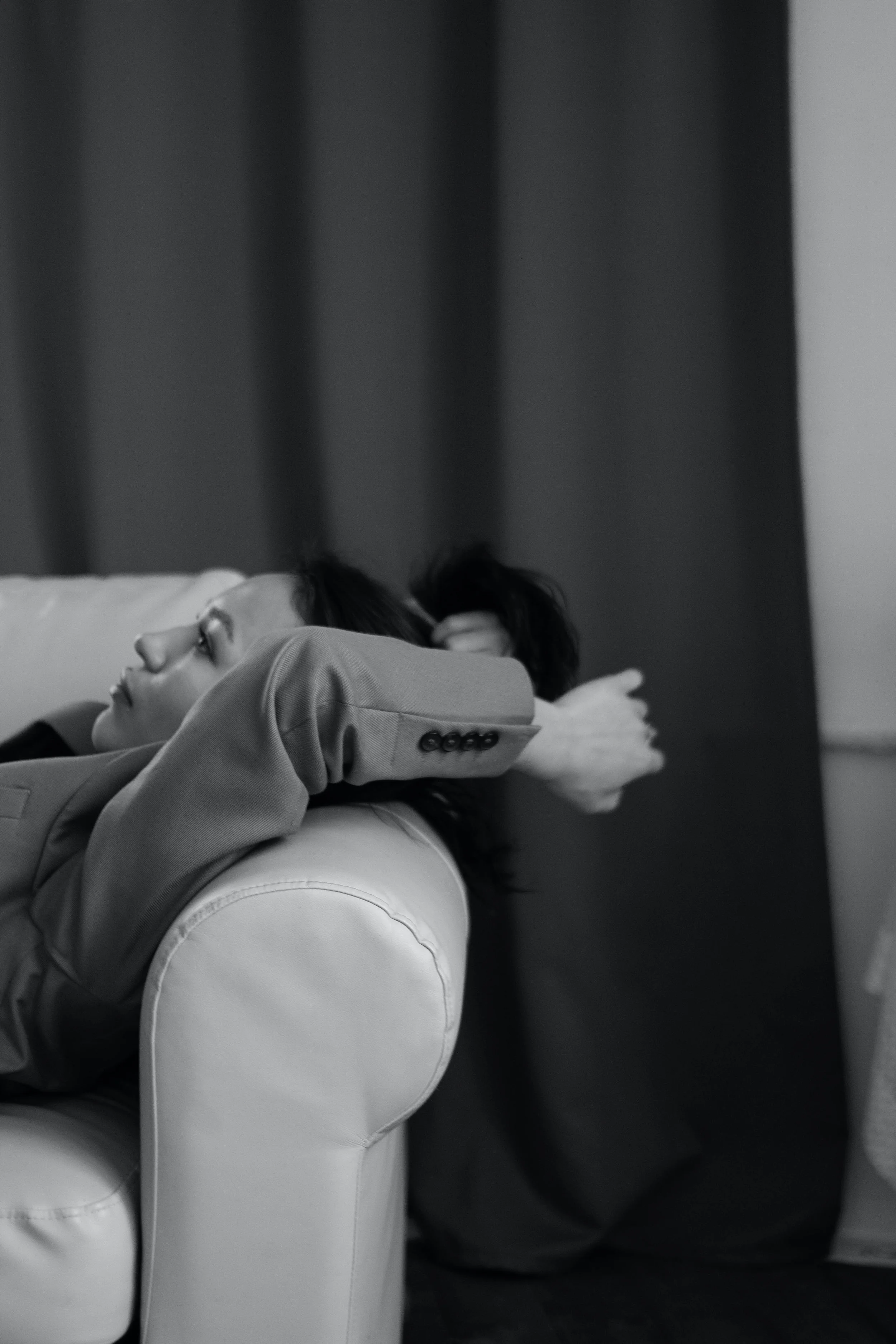 Woman lying on a couch with arms behind head, wearing a jacket, black and white photo.