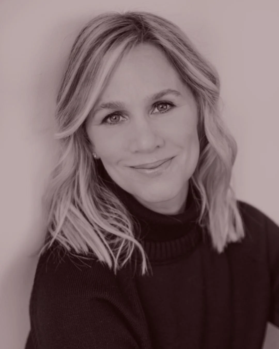 Woman in black lace outfit holding a drink with a lemon slice garnish, against a backdrop of pampas grass.