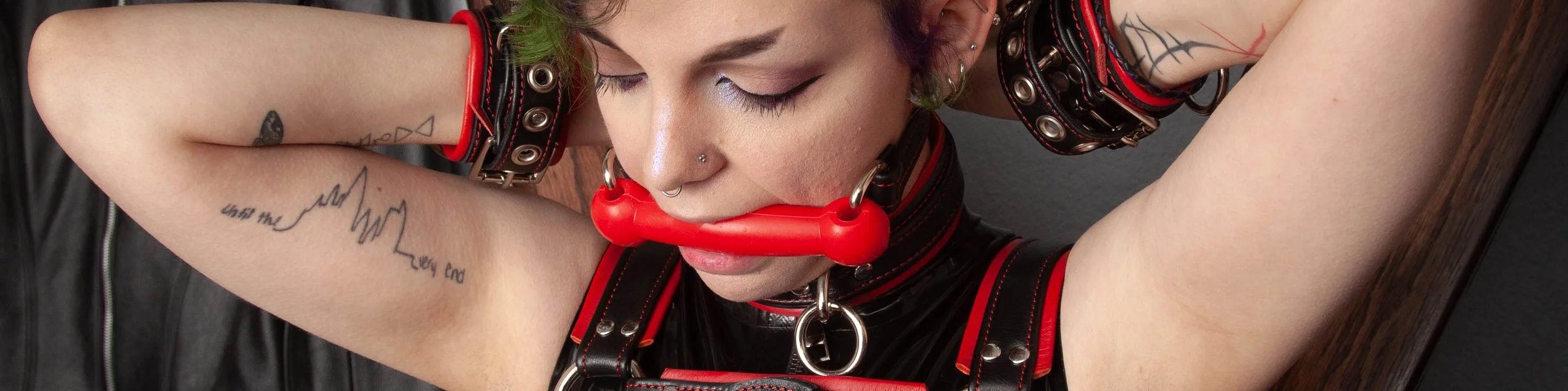 Trans man wearing a leather harness and a silicone bit gag