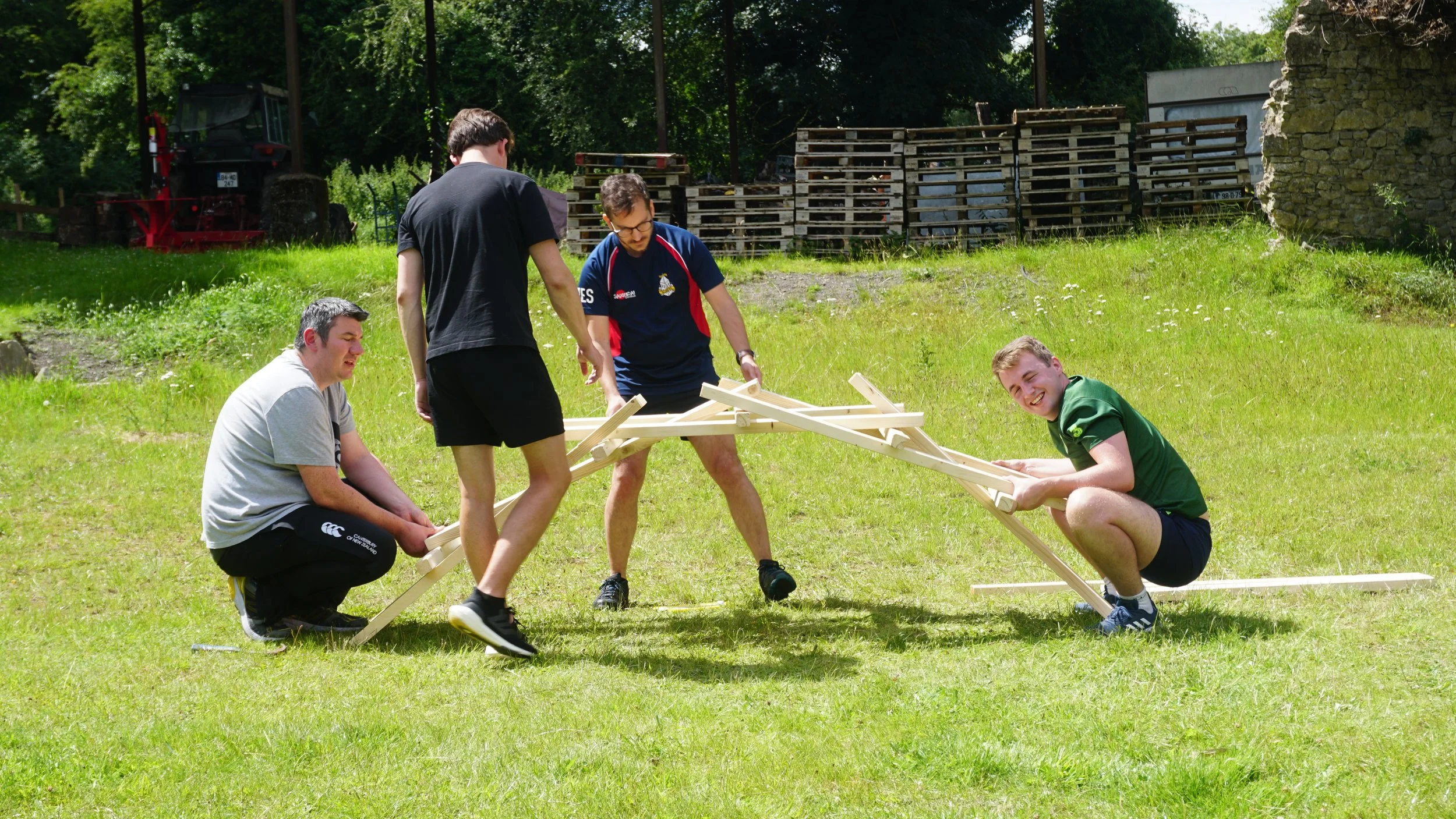 Four men assembling a wooden structure on grass outdoors