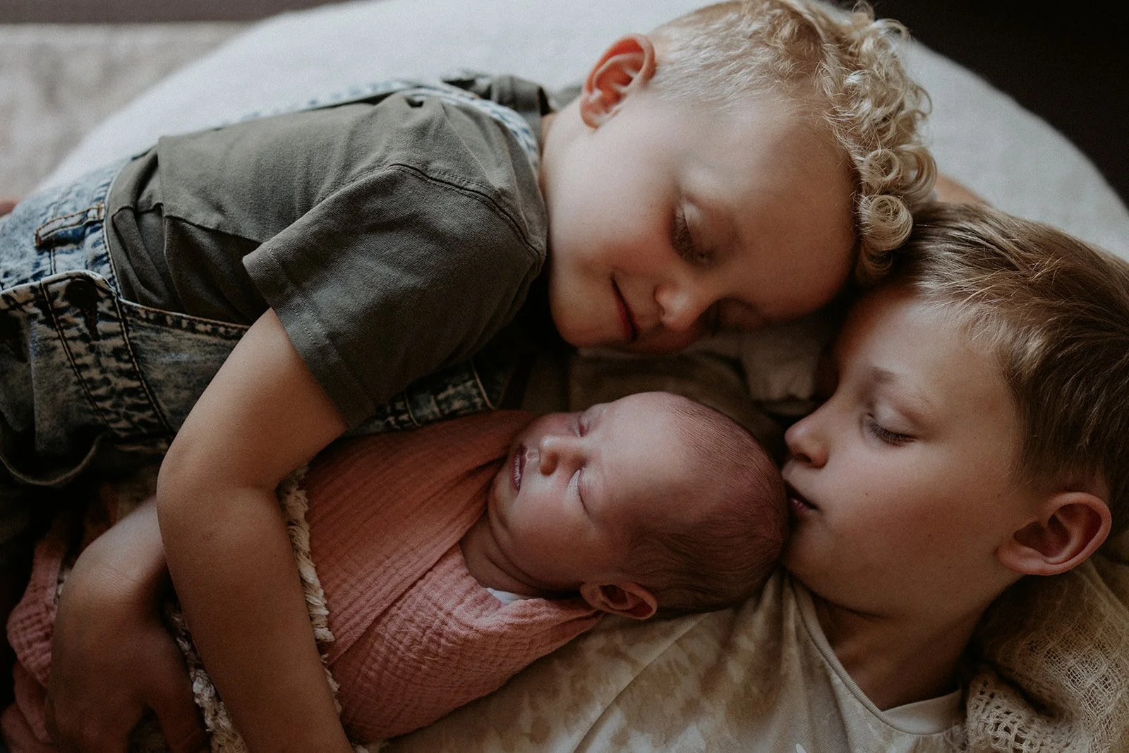 Two brother's lie next to their sleeping newborn sister. Newborn photography at its most beautiful.