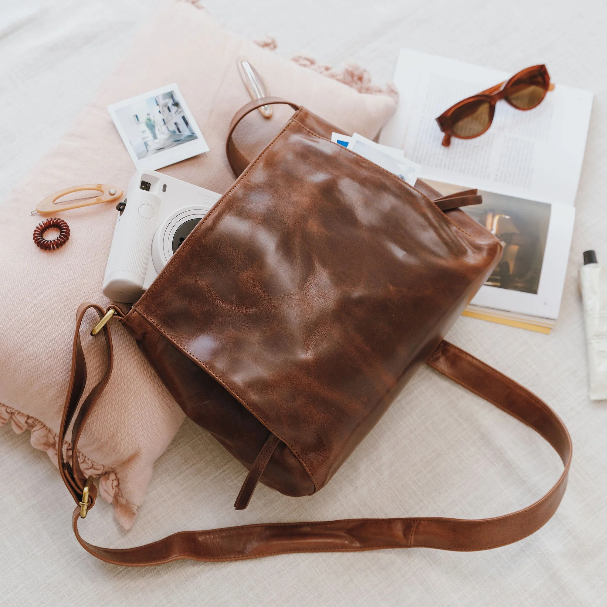 Hutton brown leather crossbody bag shown with camera and notebook showing