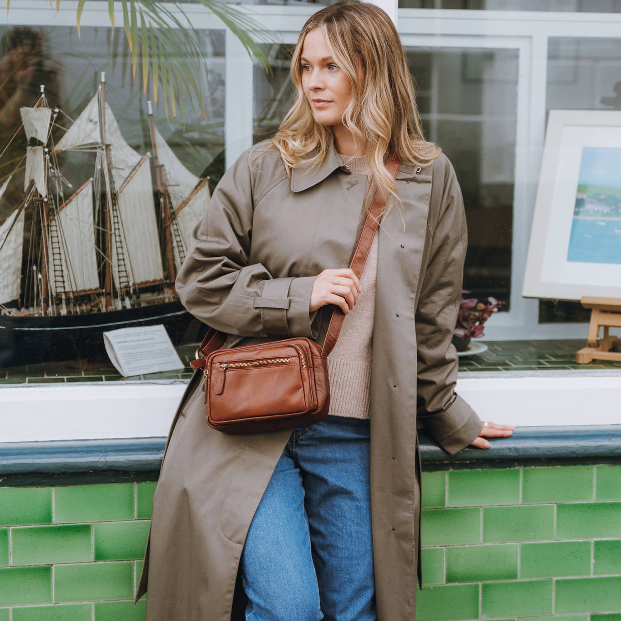 tan leather small crossbody bag worn across a model sat outside a shop