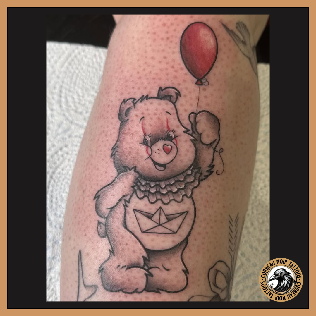 A tattoo of a cute bear holding a red balloon, with a heart on its nose, wearing a ruffled collar, and a paper boat on its belly, with some tattoo ink on the skin.