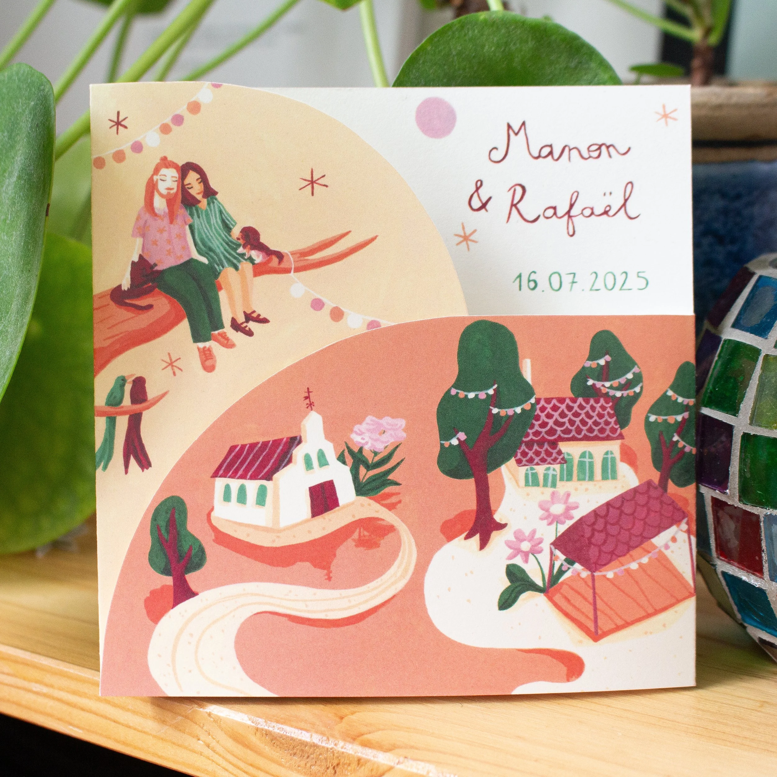 Carte d'invitation de mariage au format plié original, avec illustration colorée d'un couple assis sur une branche, décorations de fête et texte mentionnant deux prénoms et une date.