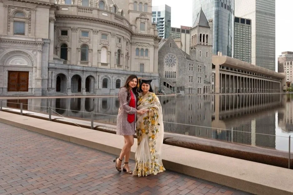 Two women standing on a promenade in front of a large historic building with a reflecting pool and modern skyscrapers in the background.