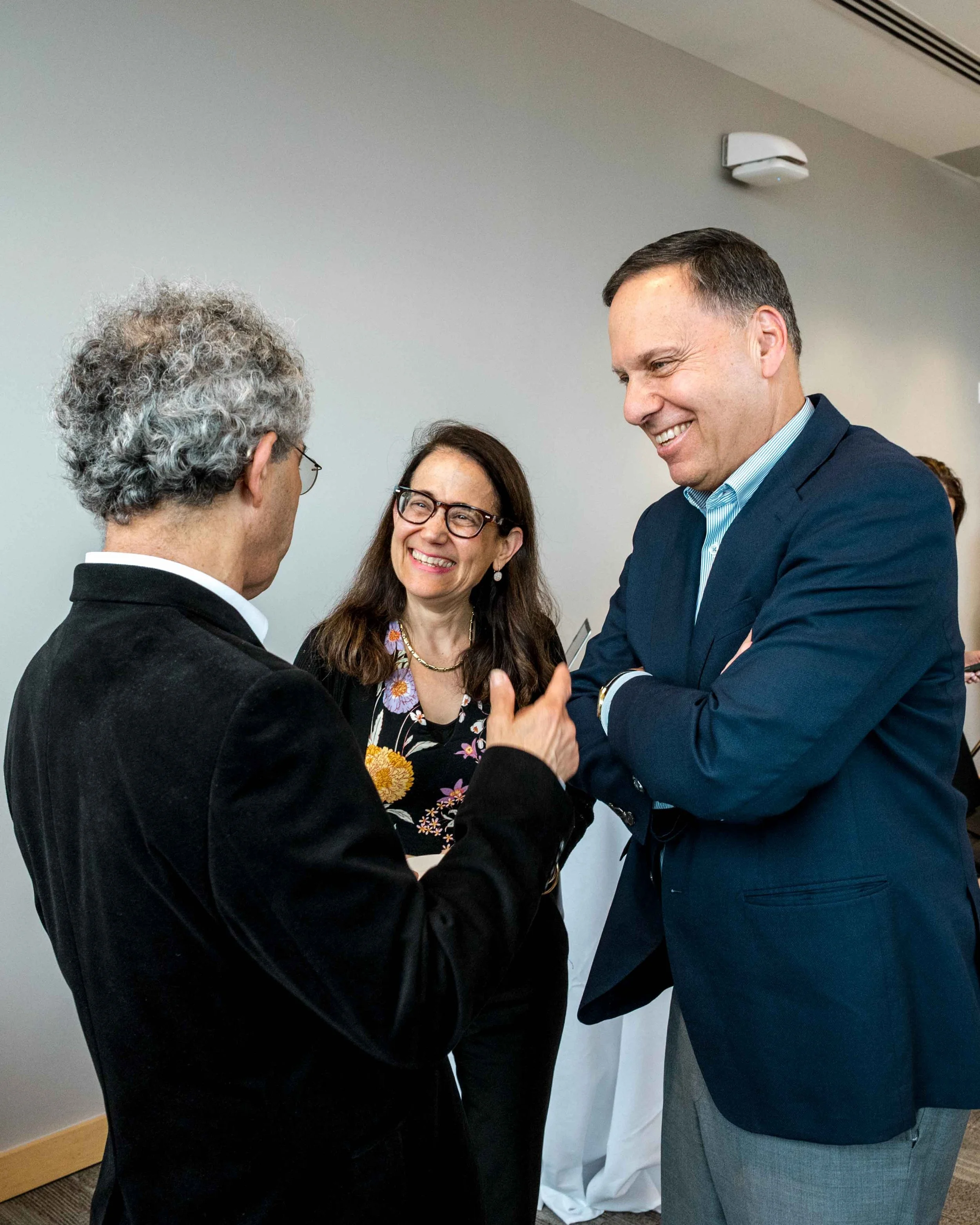Three people engaged in conversation, smiling, in a professional setting.
