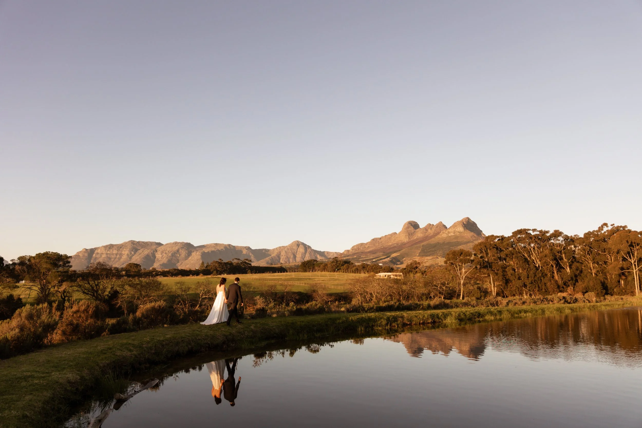 Stellenbosch Wedding Bride and Groom walking by a lake with mountain views
