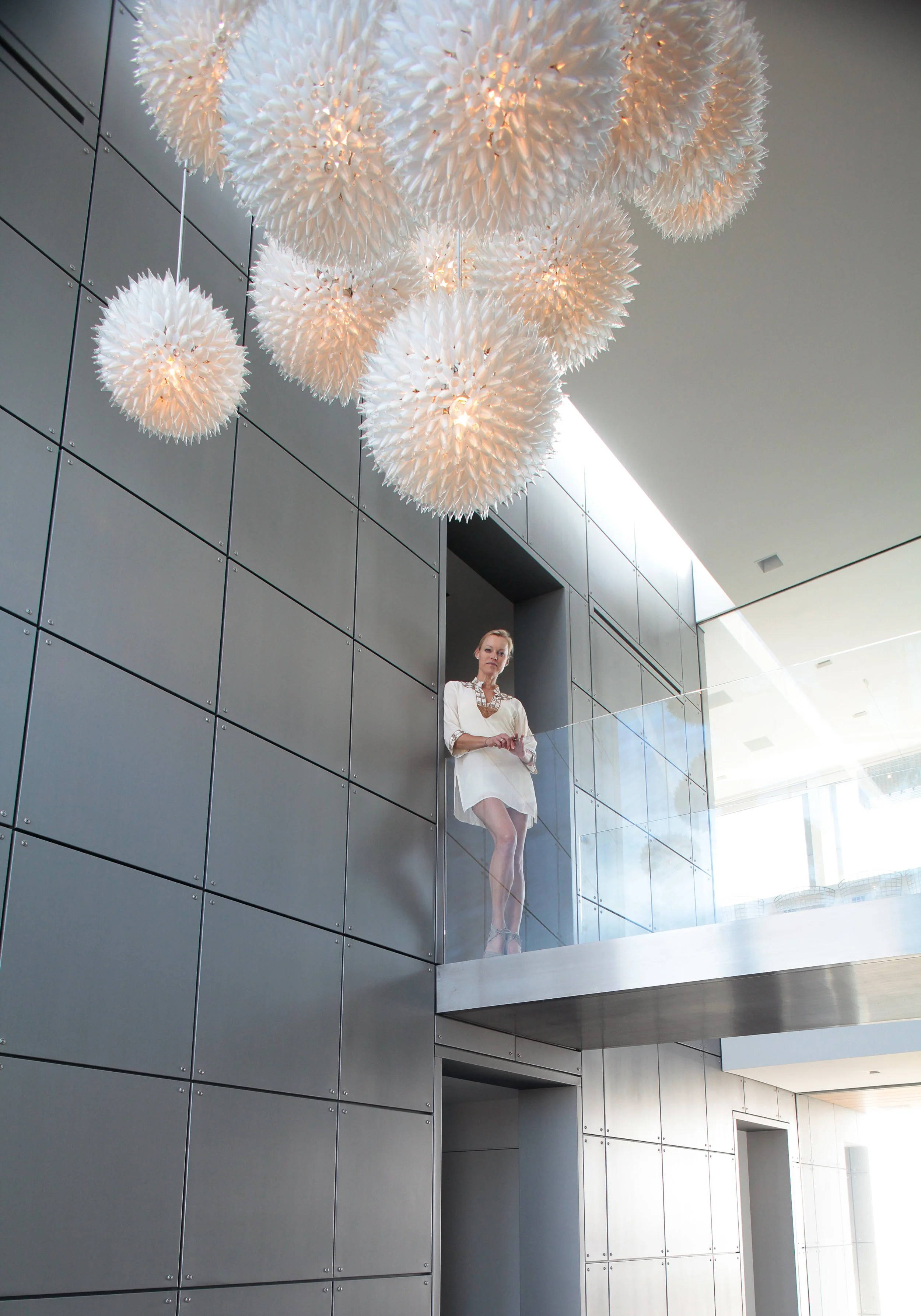 A woman standing on a balcony in a modern building with large chandeliers hanging from the ceiling.